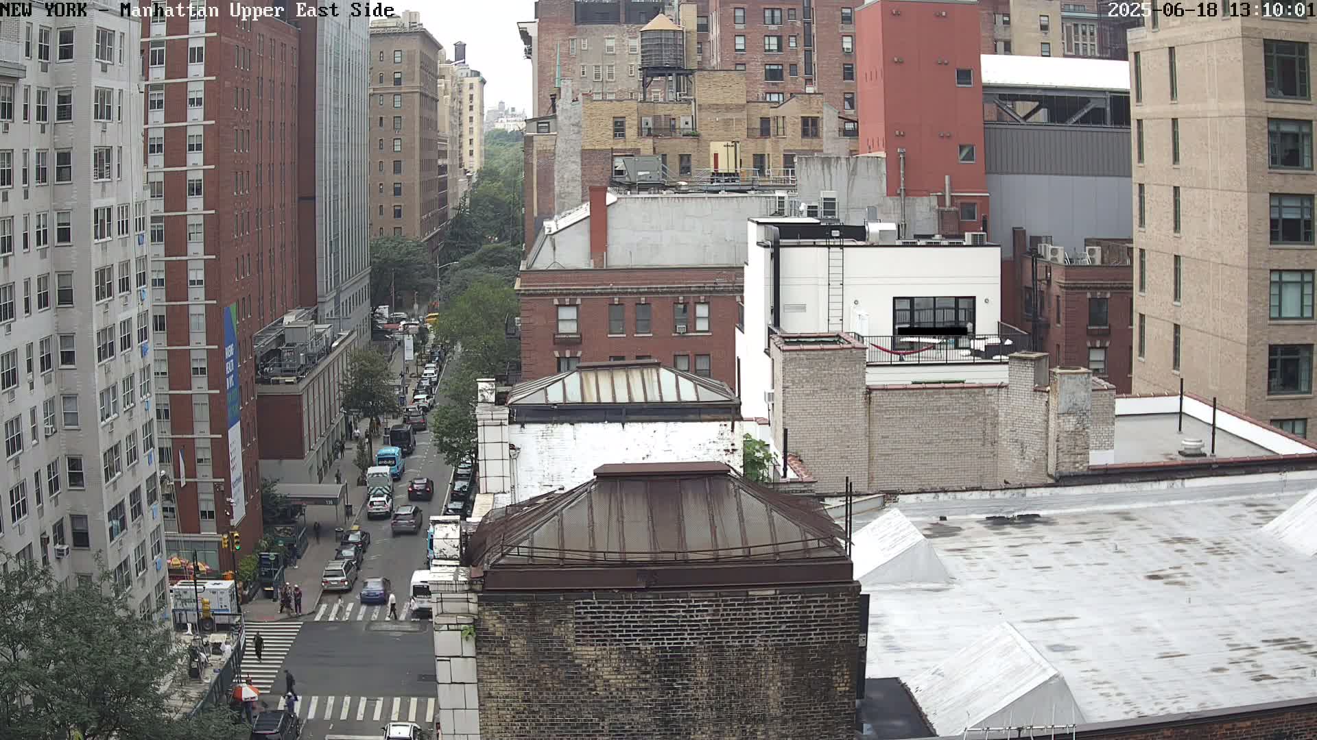 A high-angle view of a city street scene on an overcast day, showing several multi-story buildings and cars on a street below.