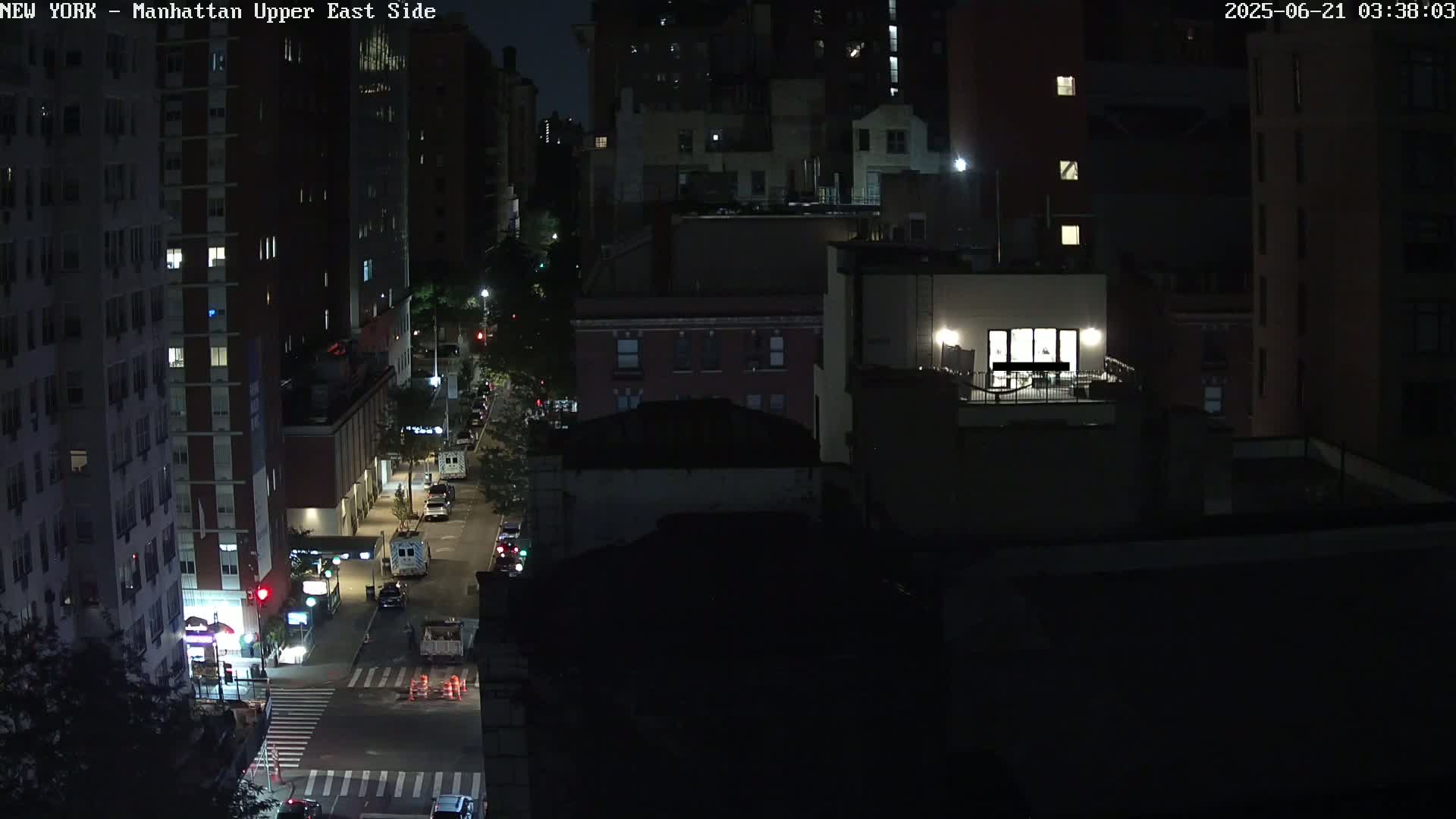 A nighttime, high-angle view shows a city street with several vehicles and buildings, some with illuminated windows.