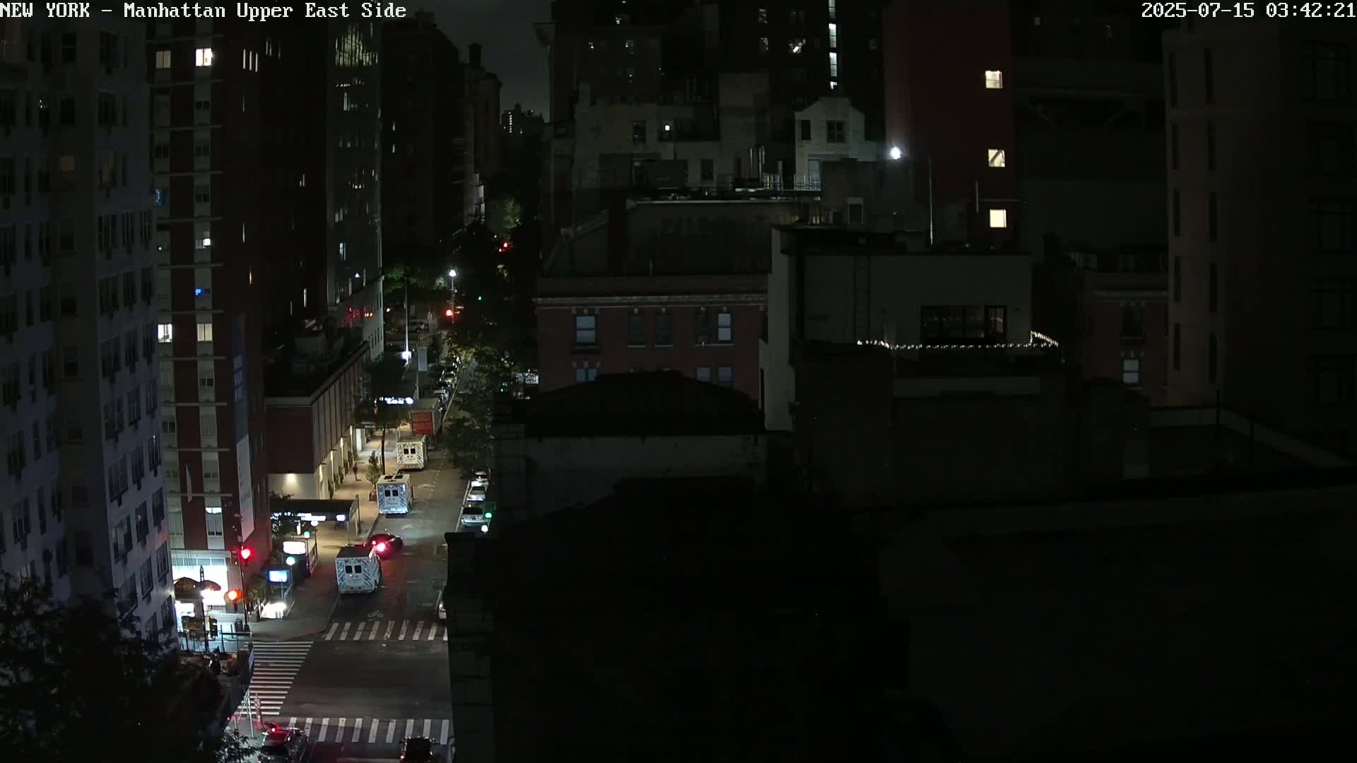 A nighttime aerial view of city streets shows a few vehicles and several multi-story buildings under dark, clear skies.