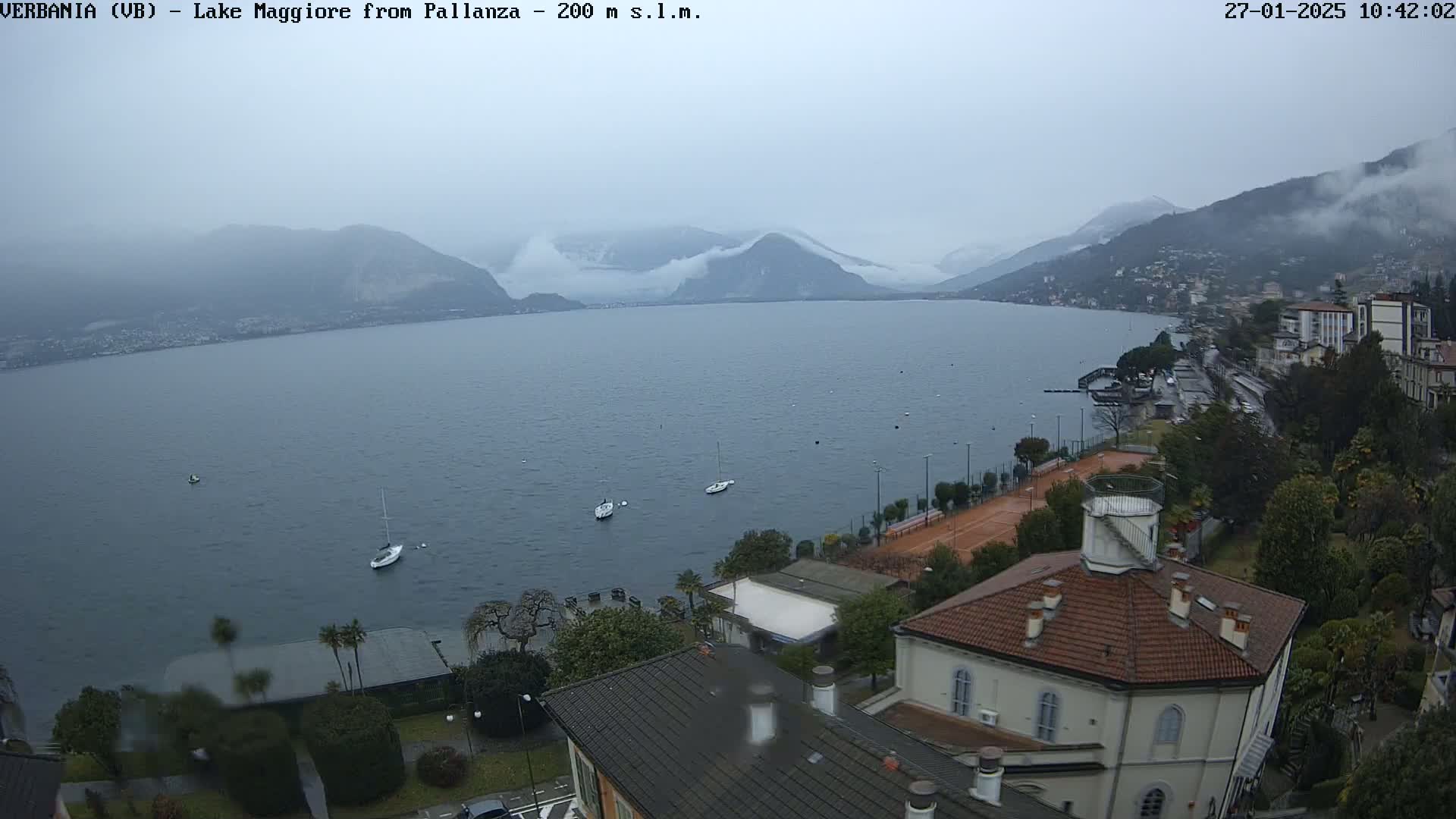 A view of Lake Maggiore from Pallanza on a cloudy day, showing a few boats on the water and buildings along the shore.