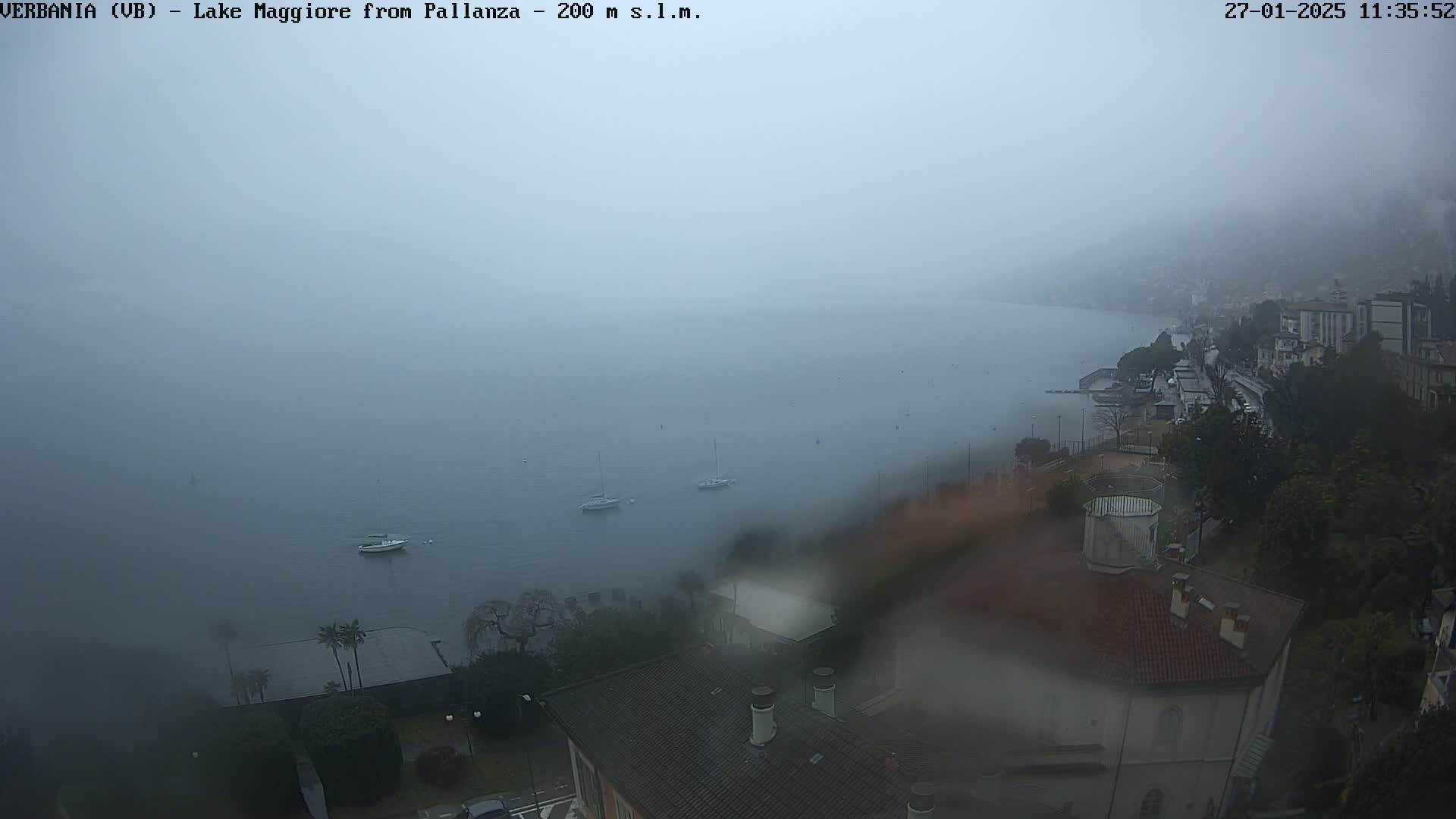 A foggy, rainy view of a lake with several boats and a town on the shoreline is seen from an elevated position.