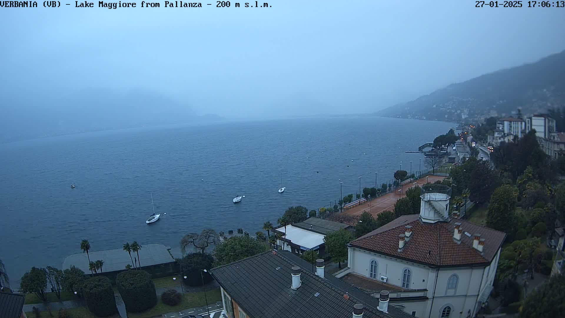 A hazy view of a lake, with a few boats and buildings along the shore, under an overcast sky.