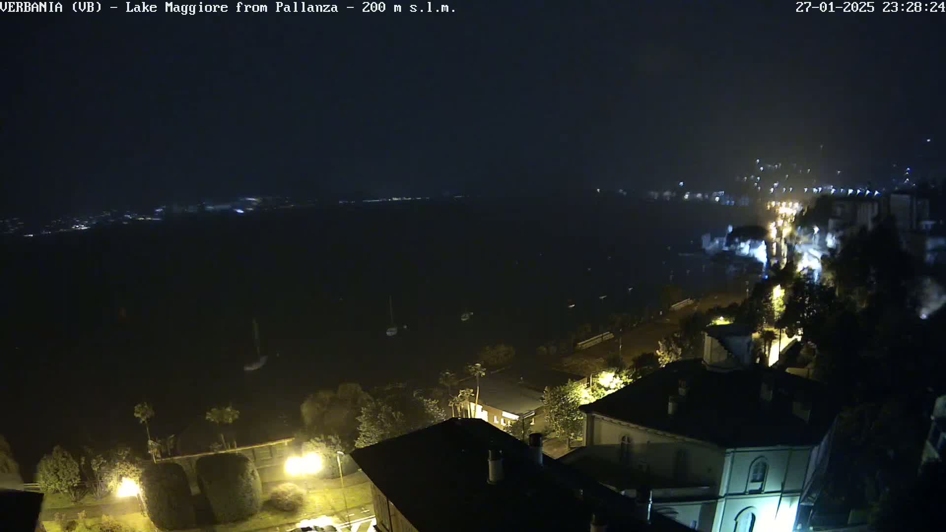 A nighttime, slightly hazy view overlooking a dark body of water with a few lights visible on the opposite shore and several illuminated buildings and streets in the foreground.
