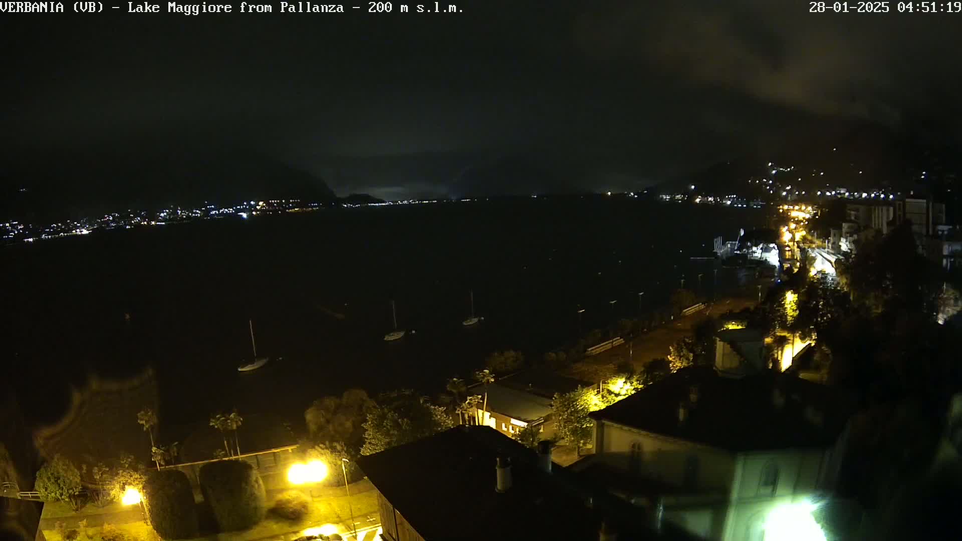 A nighttime view of a lake with a town on the shore, illuminated by streetlights under a cloudy sky.