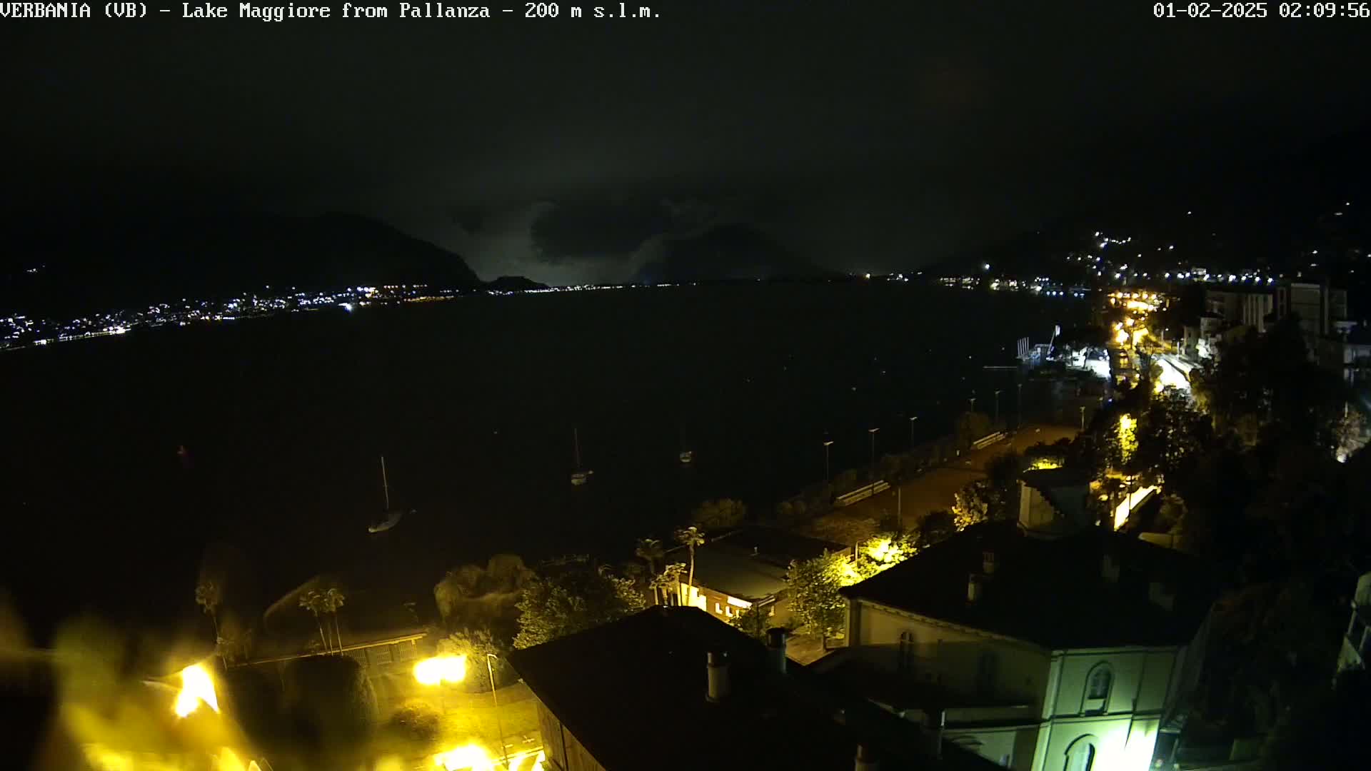 A nighttime view of a lake with a town on the shore under a dark, cloudy sky.