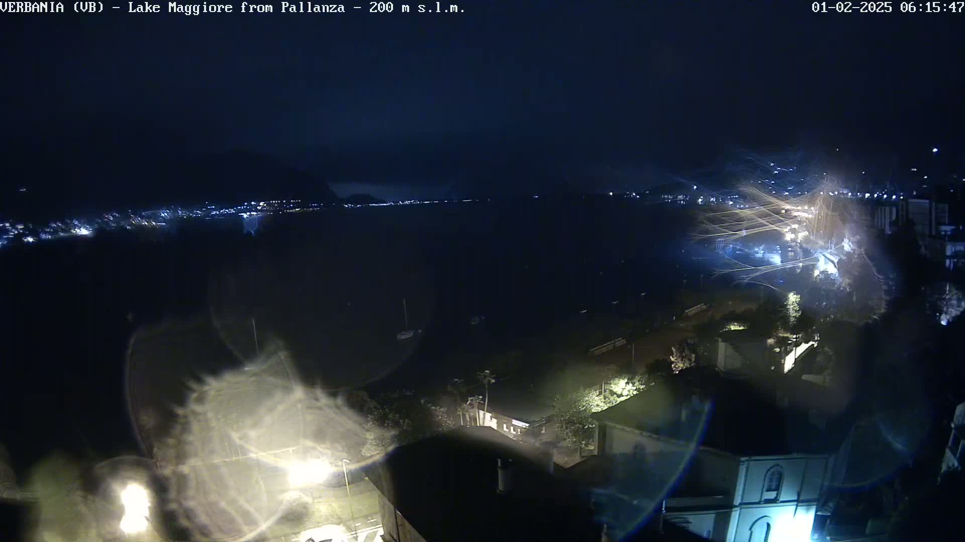 A nighttime, high-angle view of a town situated near a large body of water, with streaks of light possibly indicating rain or wind.