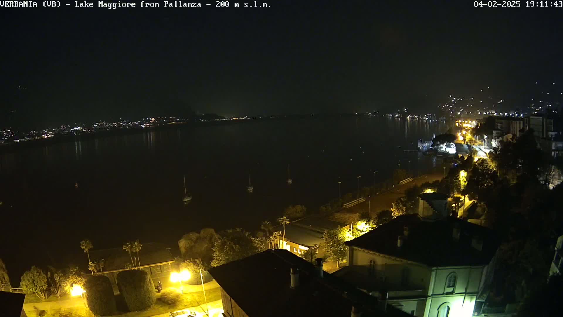 A nighttime, aerial view of a lake with several boats and a town's lights illuminating the shoreline.