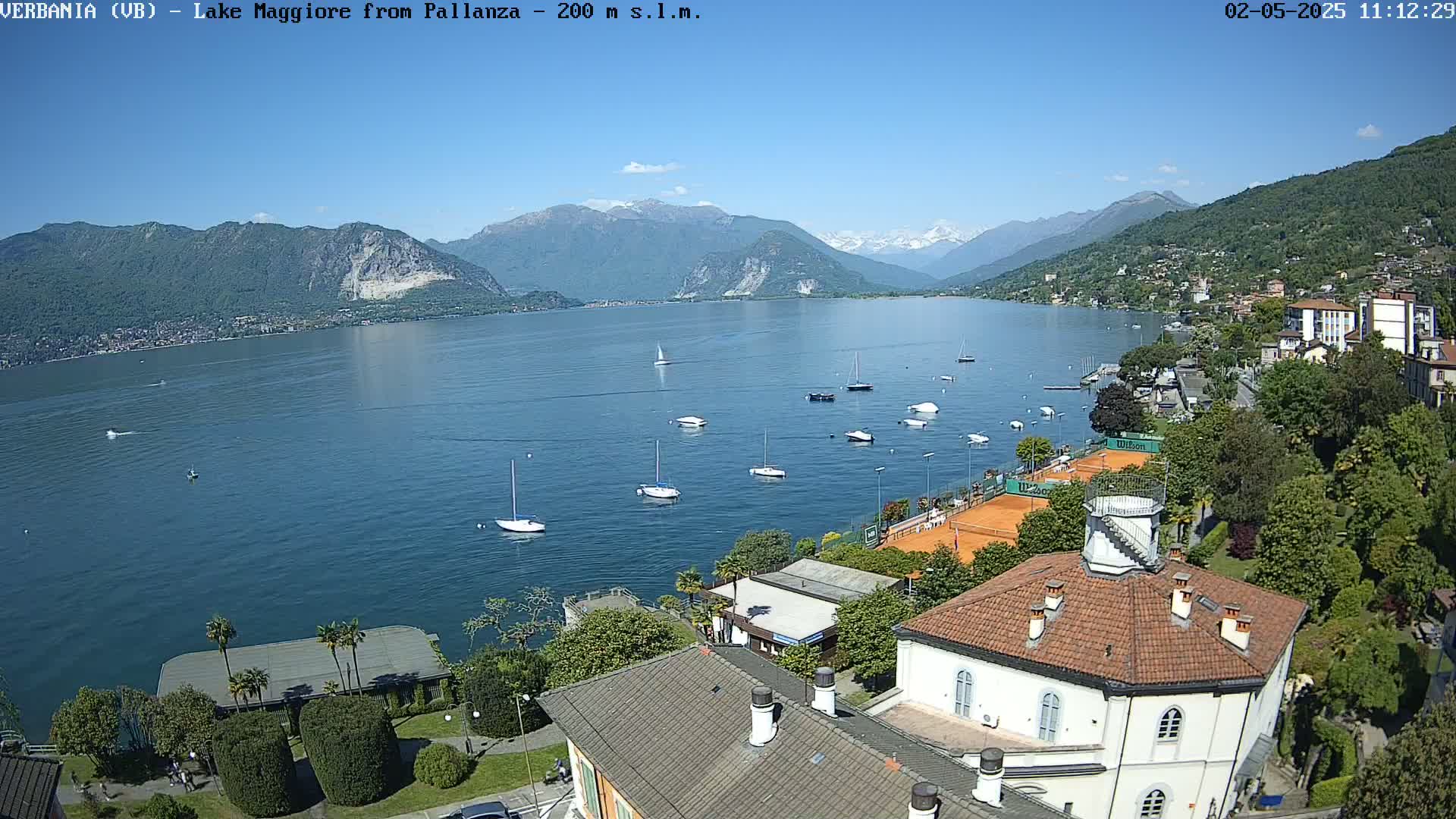 A sunny day overlooking a calm lake with sailboats and buildings, backed by mountains.