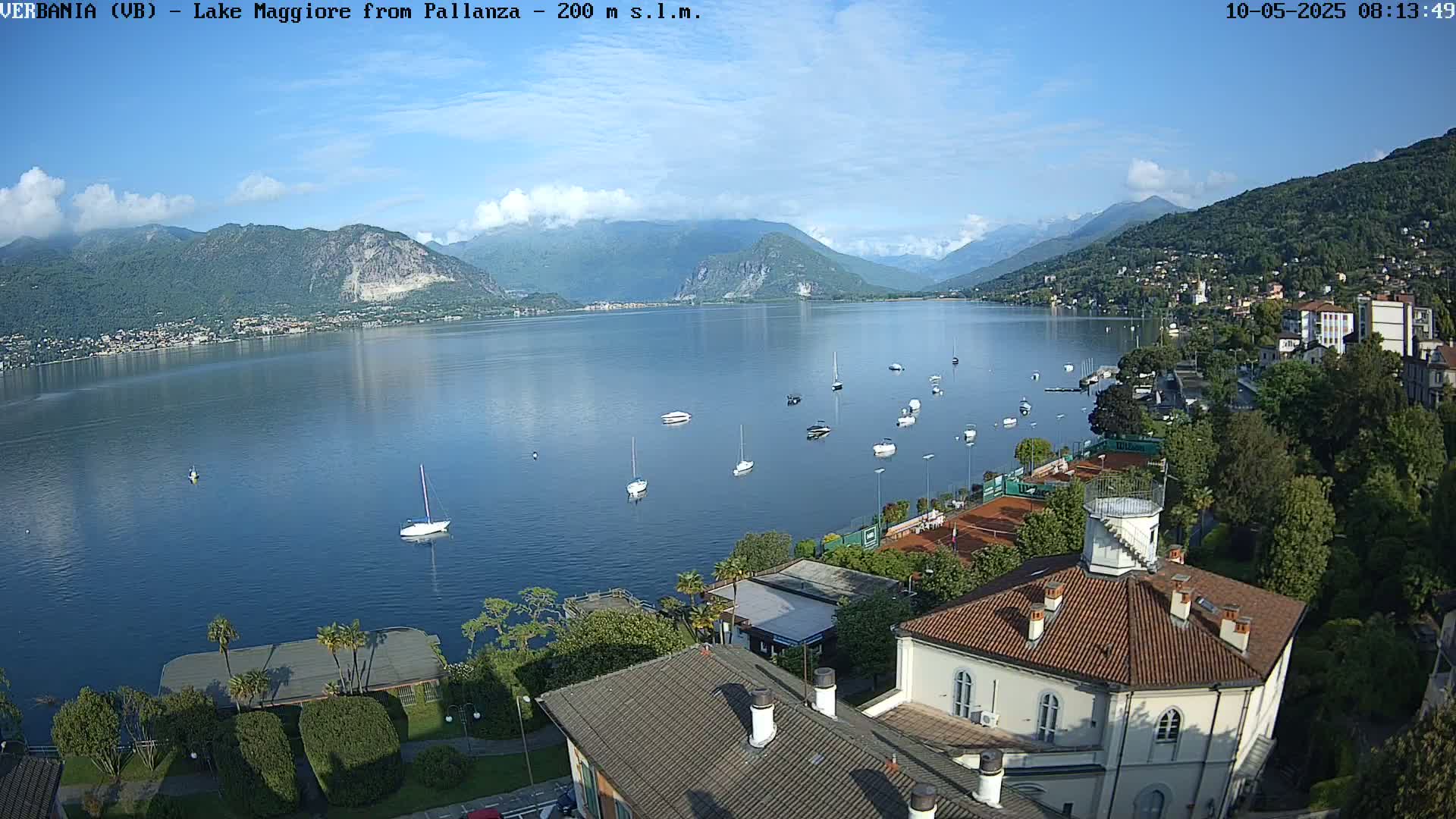 A calm lake with numerous small boats is nestled between verdant hills under a mostly sunny sky.