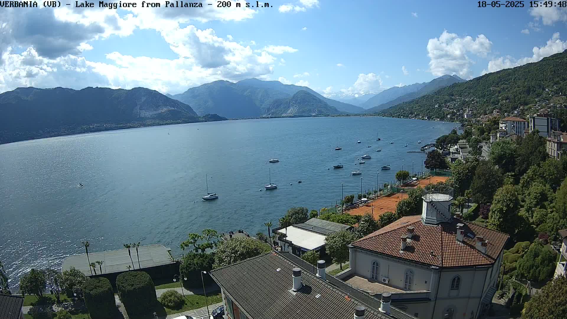 A sunny day overlooking a calm lake with numerous boats, a shoreline town, and mountains in the background.