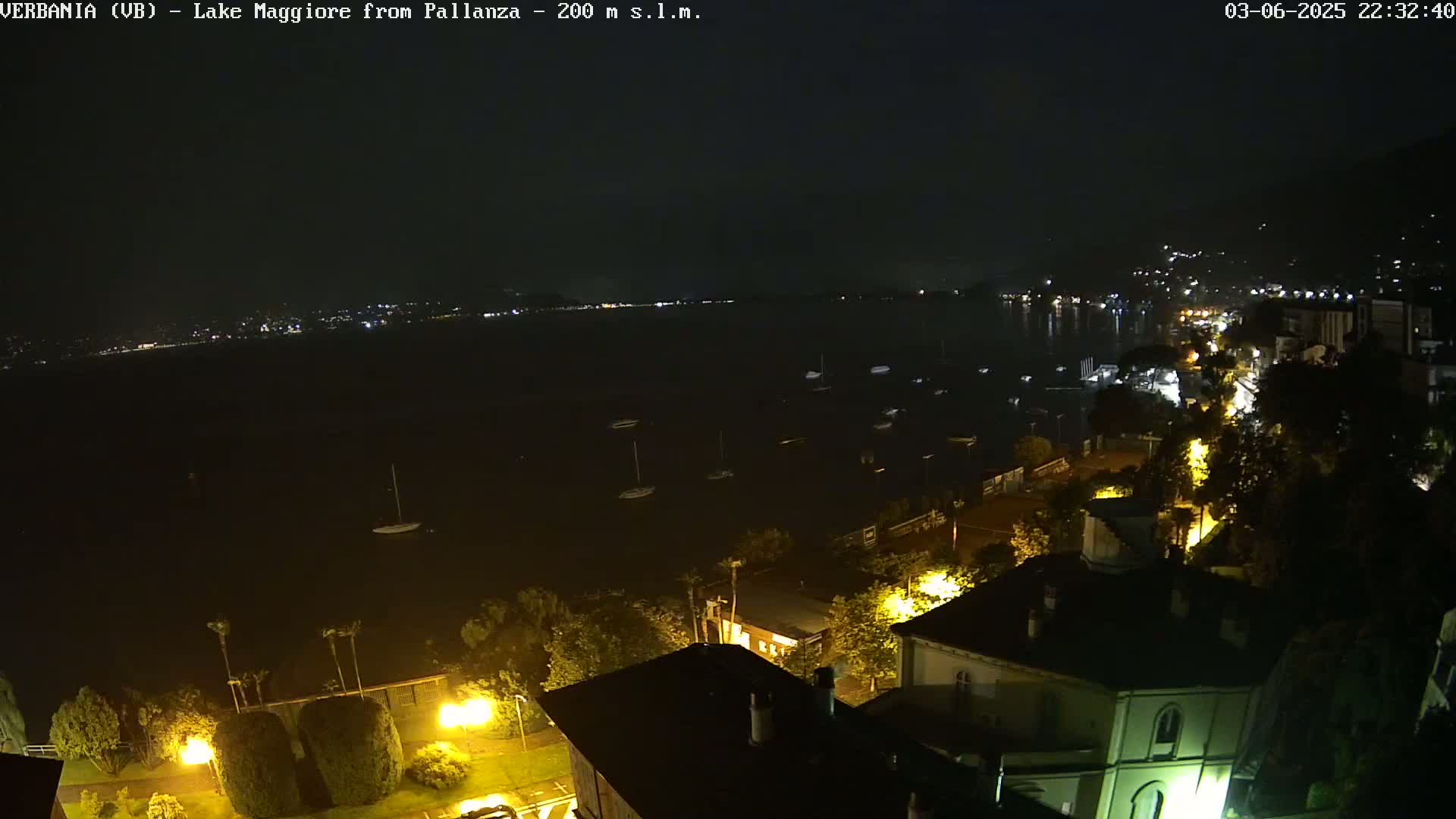 A nighttime view of a lake with boats and a town illuminated by streetlights under a clear, dark sky.
