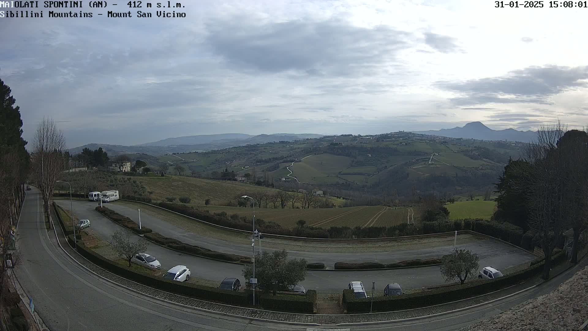 An overcast day reveals a hilly landscape with a parking lot and several cars, overlooking a sprawling valley and distant mountains.