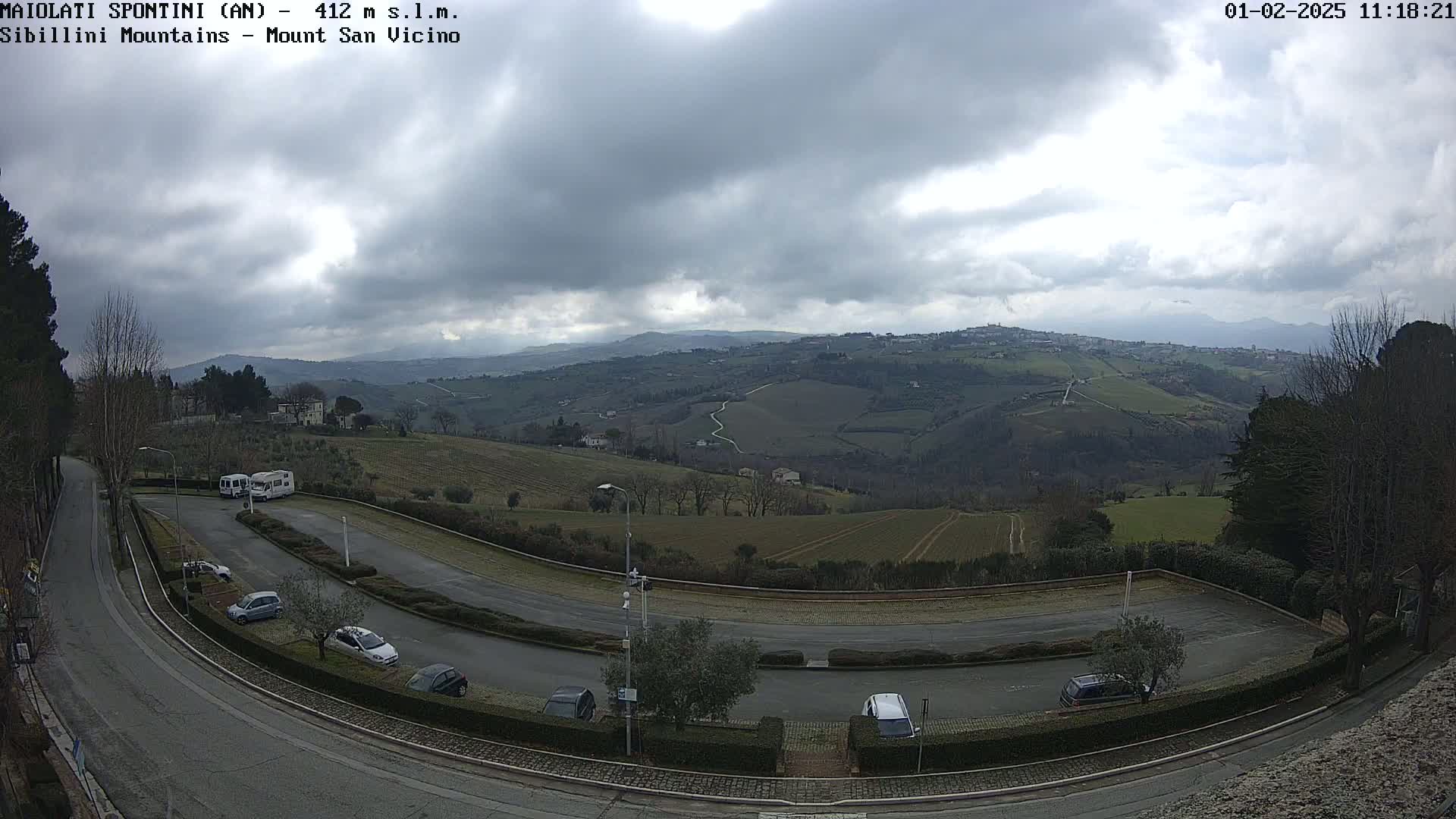 A parking lot with several cars and RVs overlooks a hilly landscape under a cloudy sky.