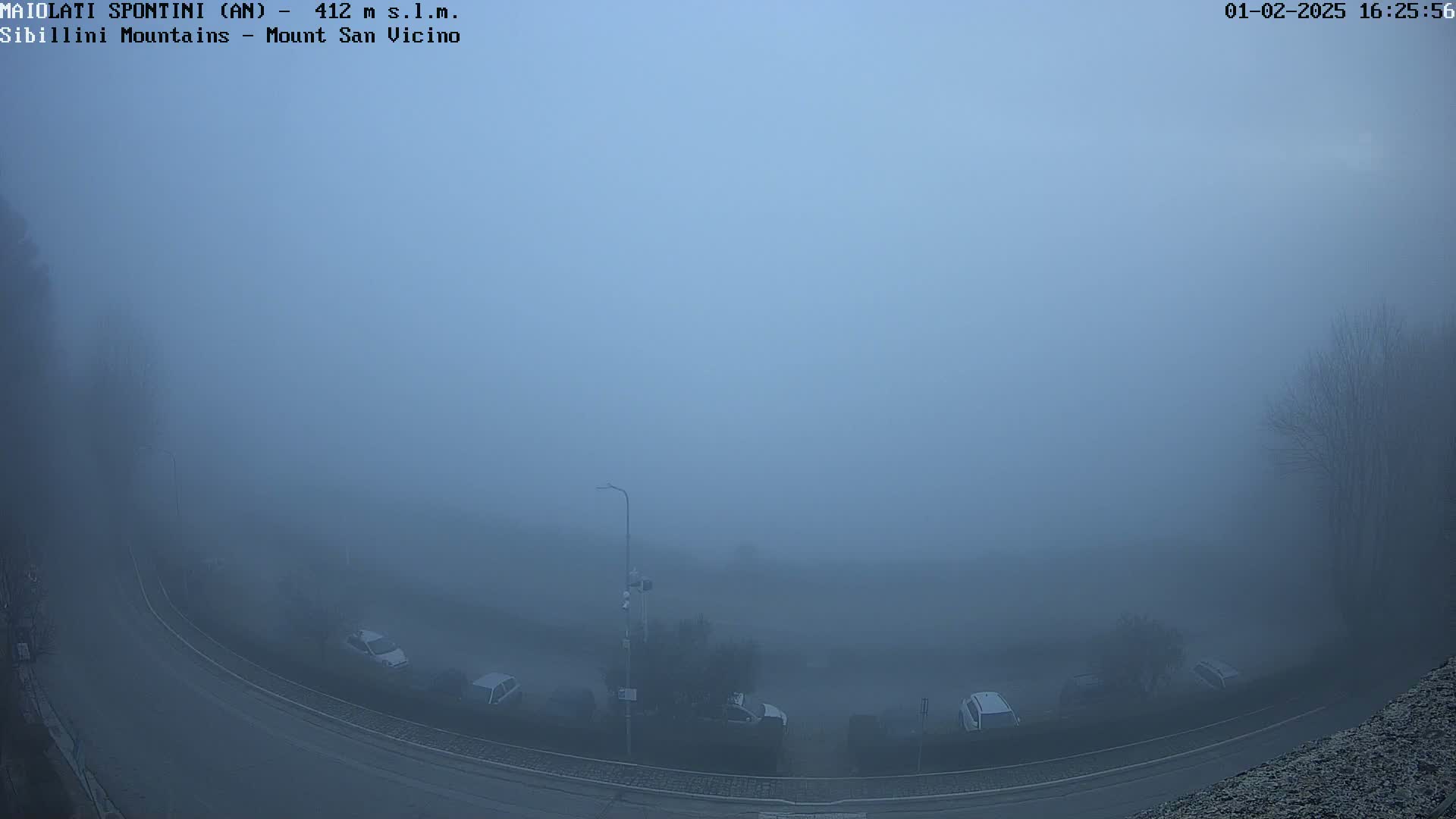 A thick fog obscures a view of a curved road and several parked cars in a parking lot.