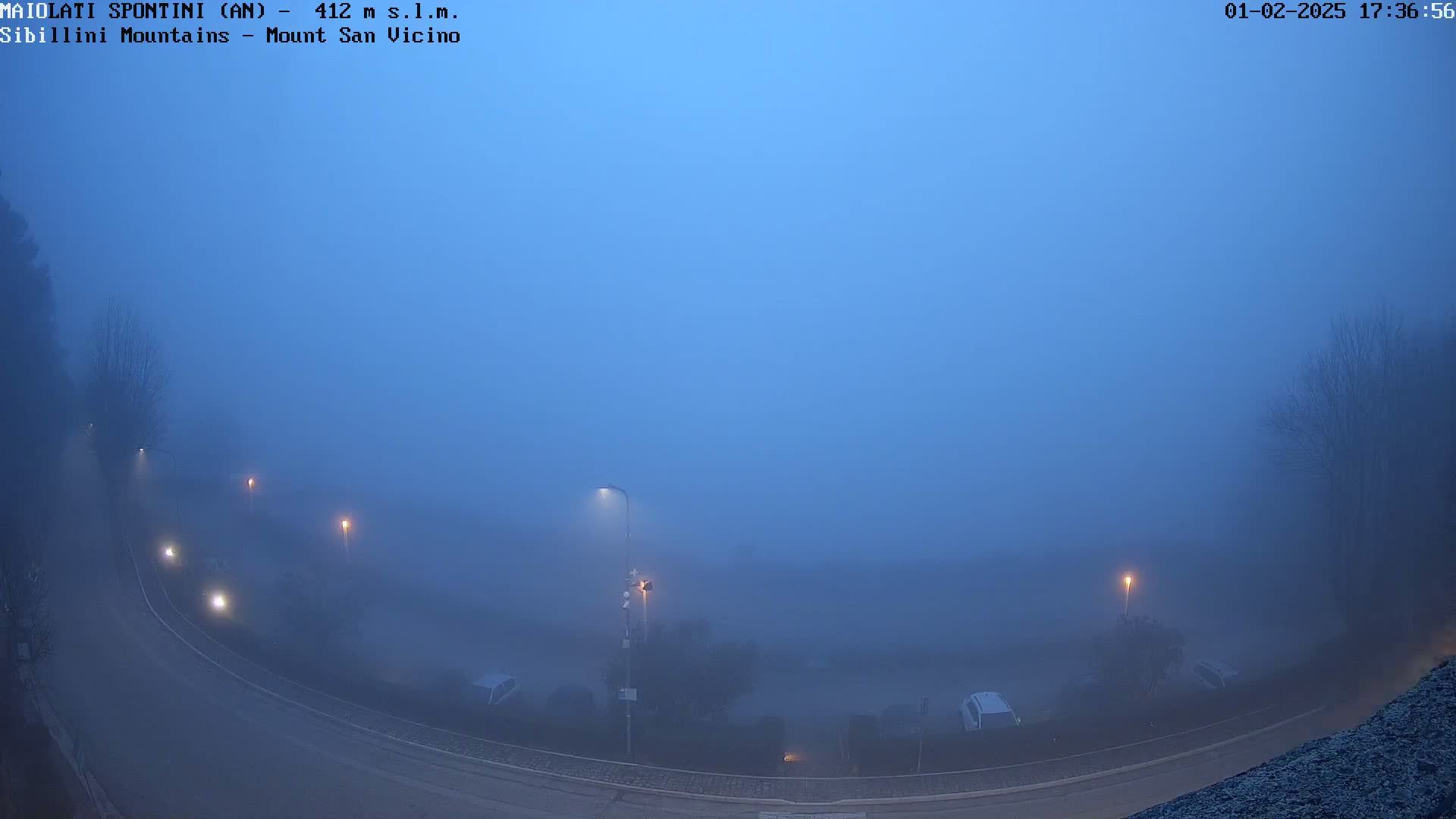 A foggy, dusk scene shows a curving road with cars and streetlights, visible through a thick layer of fog.
