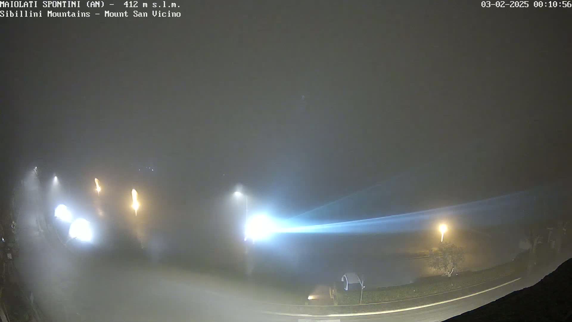 A foggy night scene shows a road with vehicle headlights and streetlights visible through the mist.