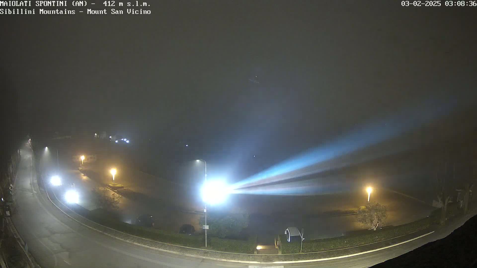 A foggy night scene shows a curved road with cars and streetlights, illuminated by a bright beam of light cutting across the scene.