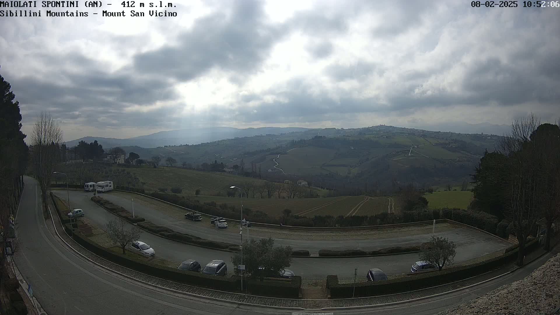 A parking lot with several cars and RVs overlooks a hilly landscape under a cloudy sky.