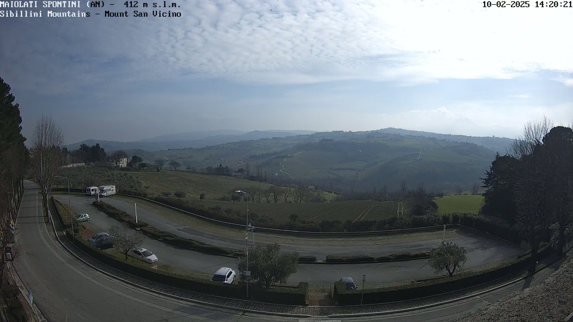 A mostly sunny day reveals a view of rolling hills, farmland, and a parking lot with several cars and RVs, all under a slightly hazy sky.
