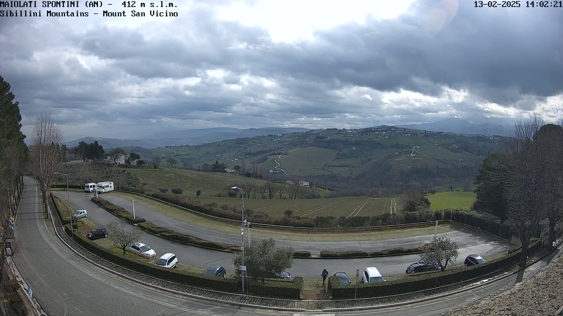 A winding road curves through a parking lot overlooking a hilly landscape under a cloudy sky.