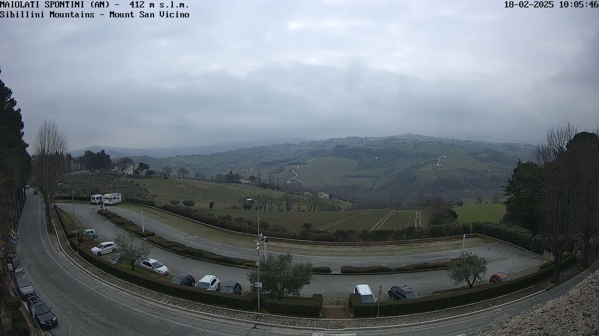 A winding road curves through a parking lot overlooking a hilly landscape under an overcast sky.