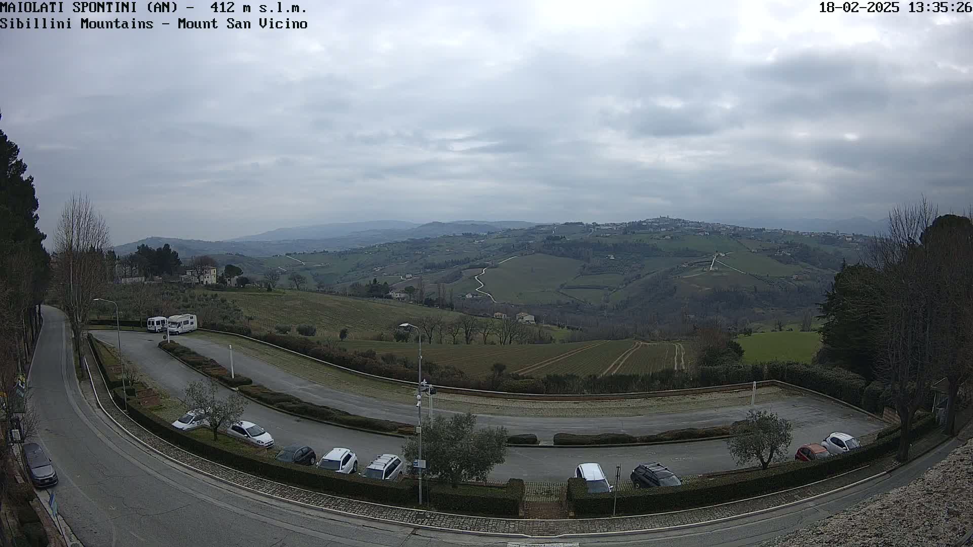 A parking lot with several cars and RVs overlooks a hilly landscape under a cloudy sky.