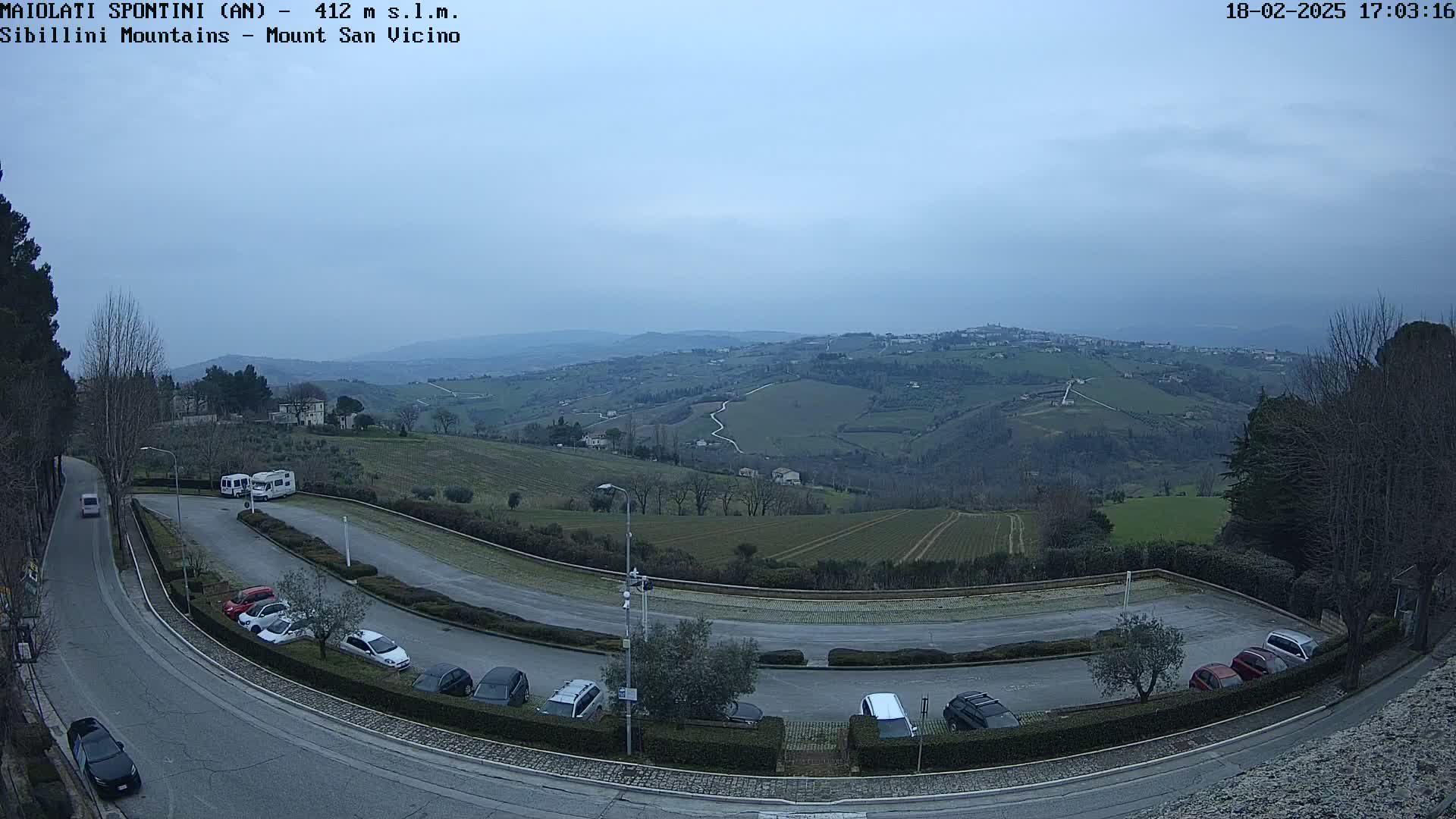A parking lot with several cars and RVs overlooks a hilly landscape under an overcast sky.