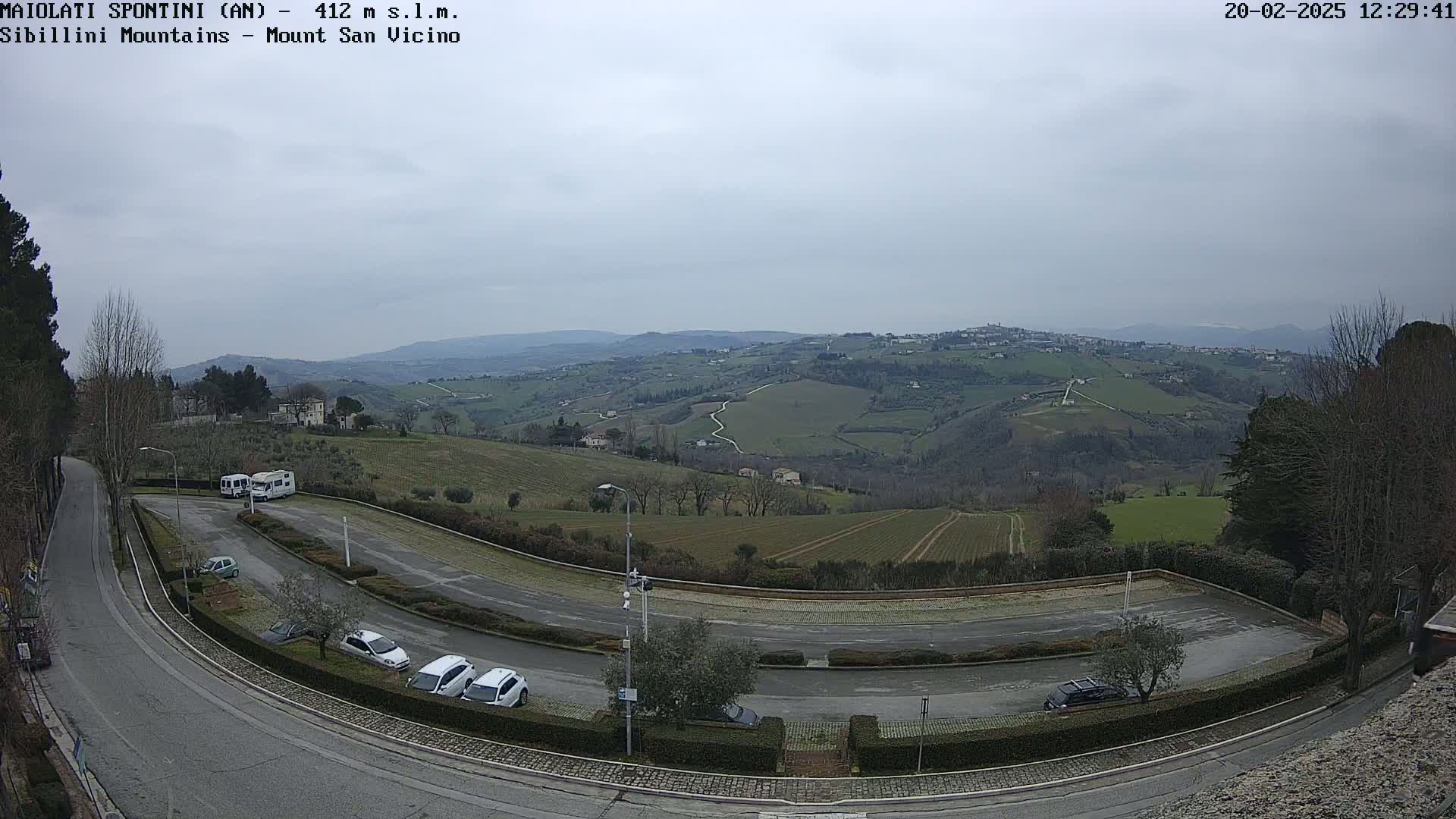 A high-angle view of a parking lot with several cars and RVs, overlooking a hilly landscape under an overcast sky.