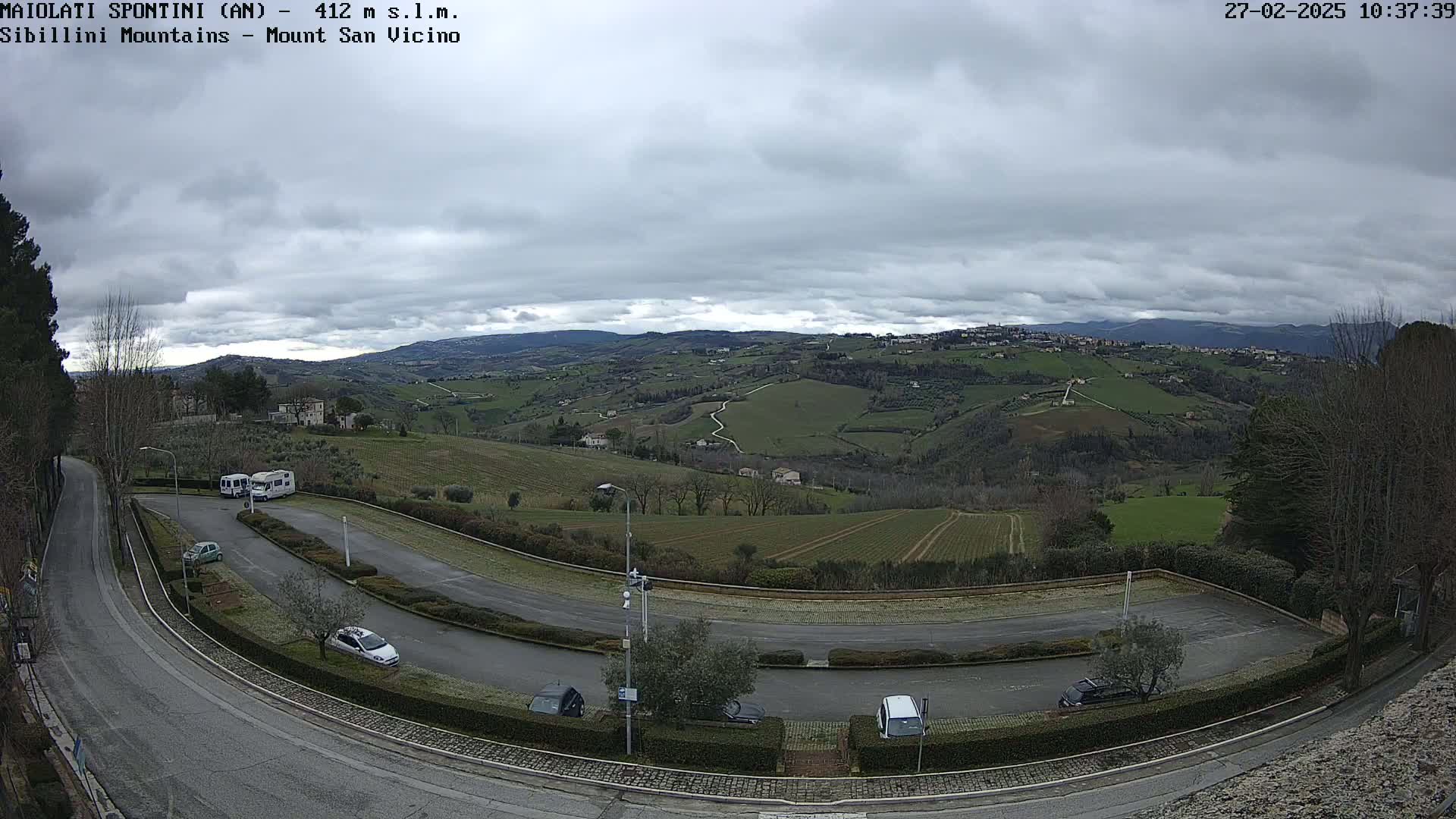 A parking lot with several cars and RVs overlooks a hilly landscape under an overcast sky.