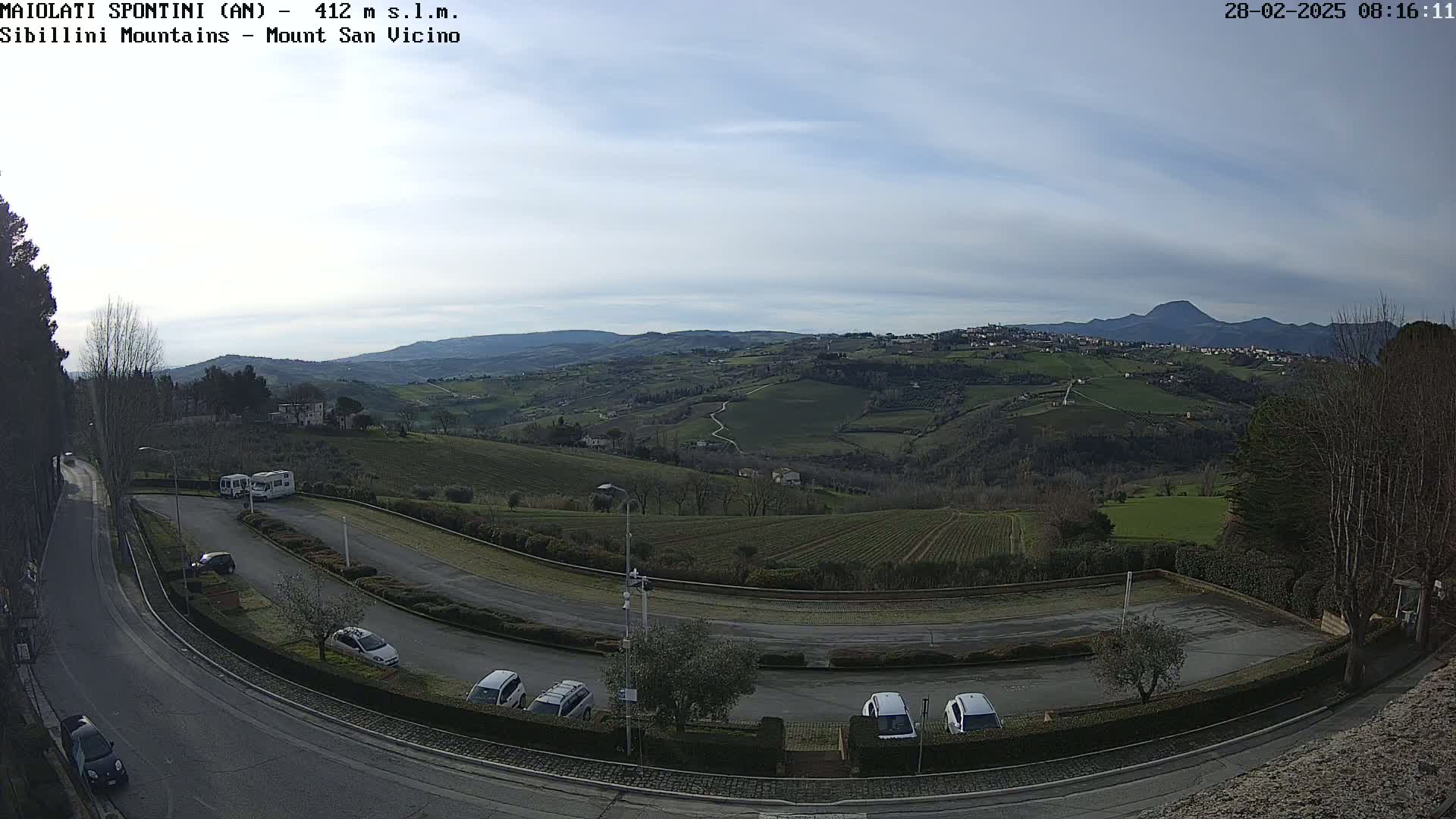 A mostly clear, daytime view of a parking lot and winding road overlooking rolling hills and distant mountains.