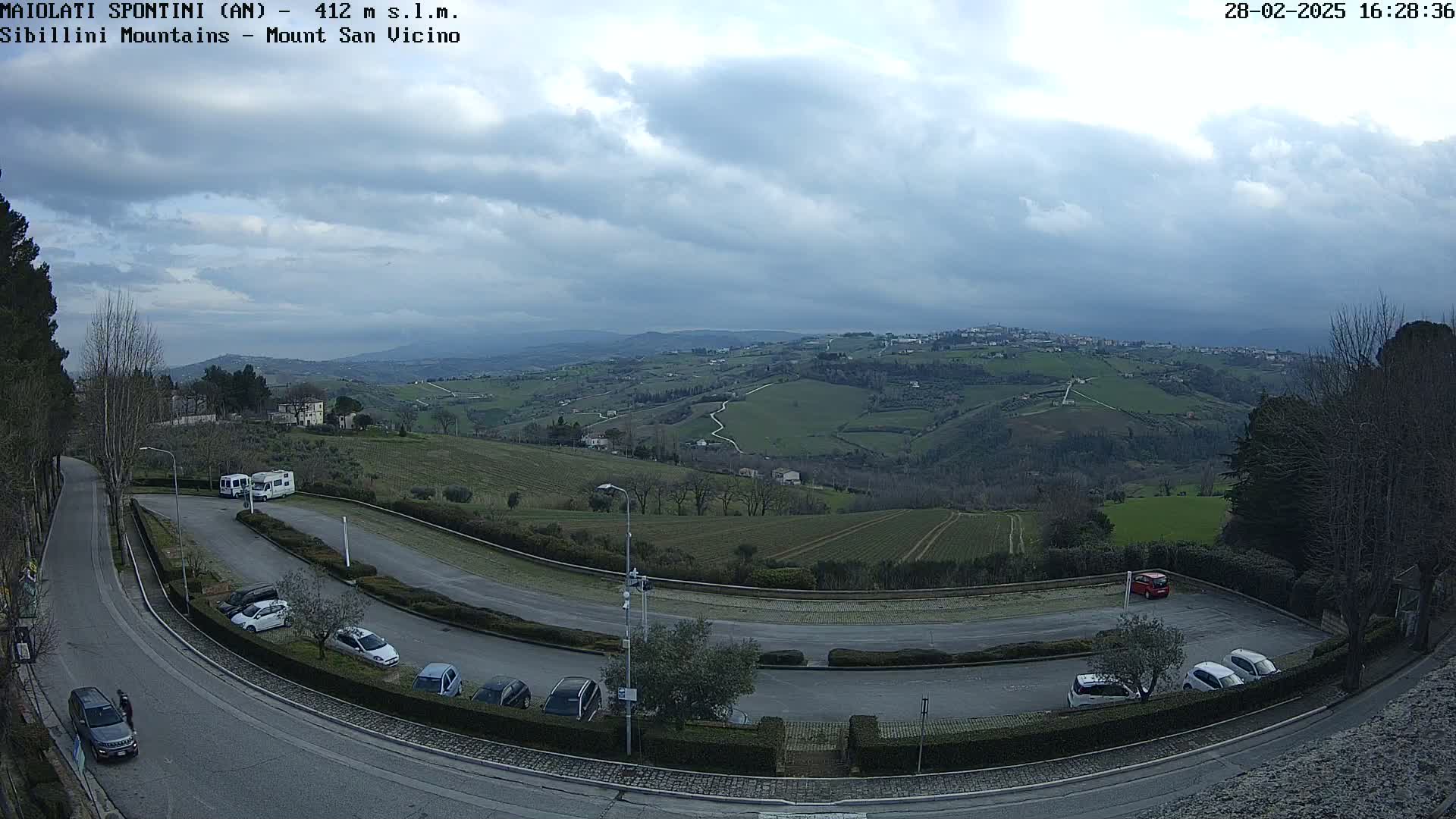 A parking lot with several cars and RVs overlooks a hilly landscape under a cloudy sky.