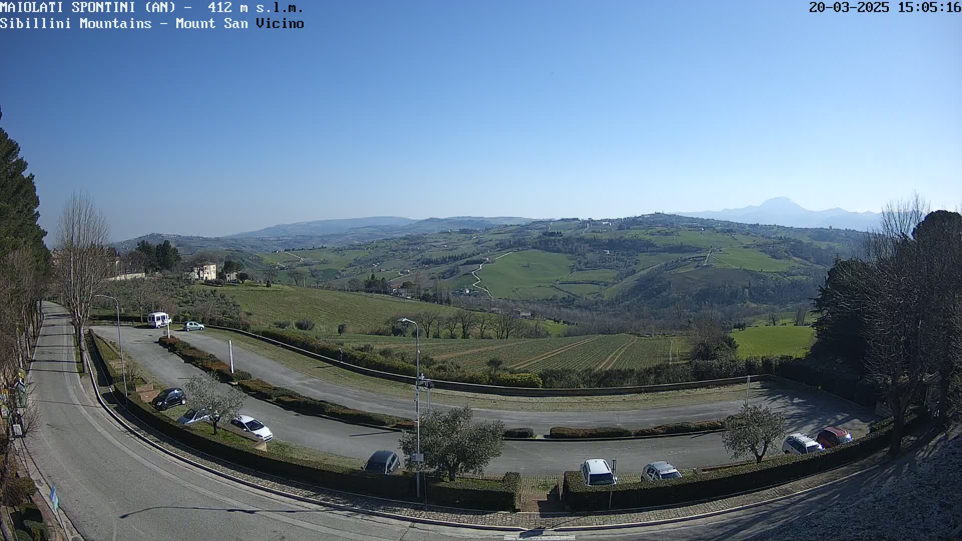 A parking lot with several cars overlooks a vast, hilly landscape under a clear blue sky.