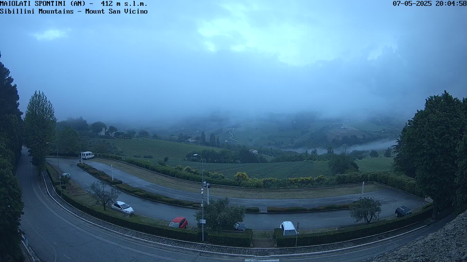 A misty, hilly landscape with a winding road and a few cars parked in a lot is visible from an elevated viewpoint.
