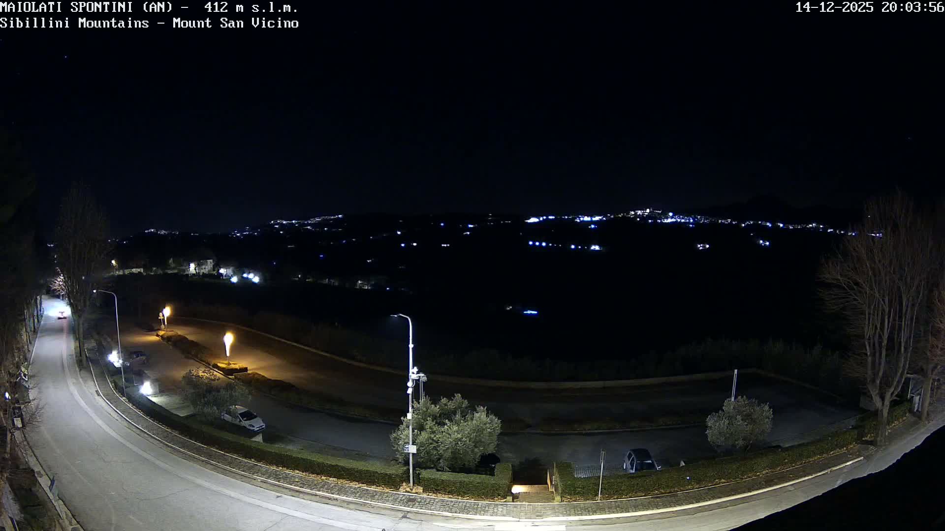 A foggy and overcast outdoor scene features a winding road with parked cars in the foreground, overlooking rolling hills and cultivated fields that fade into the distant mist.