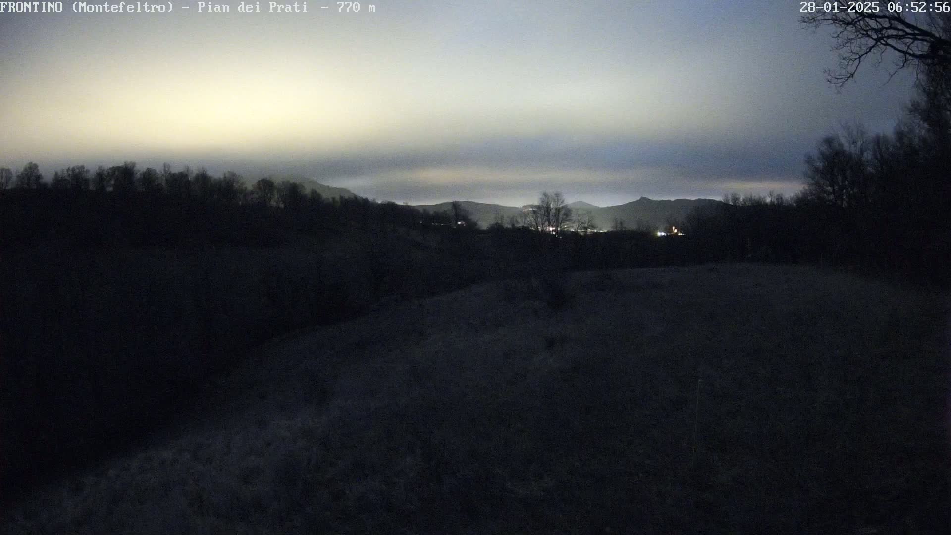A dark, hilly landscape is visible under a twilight sky, with faint lights illuminating a distant town.