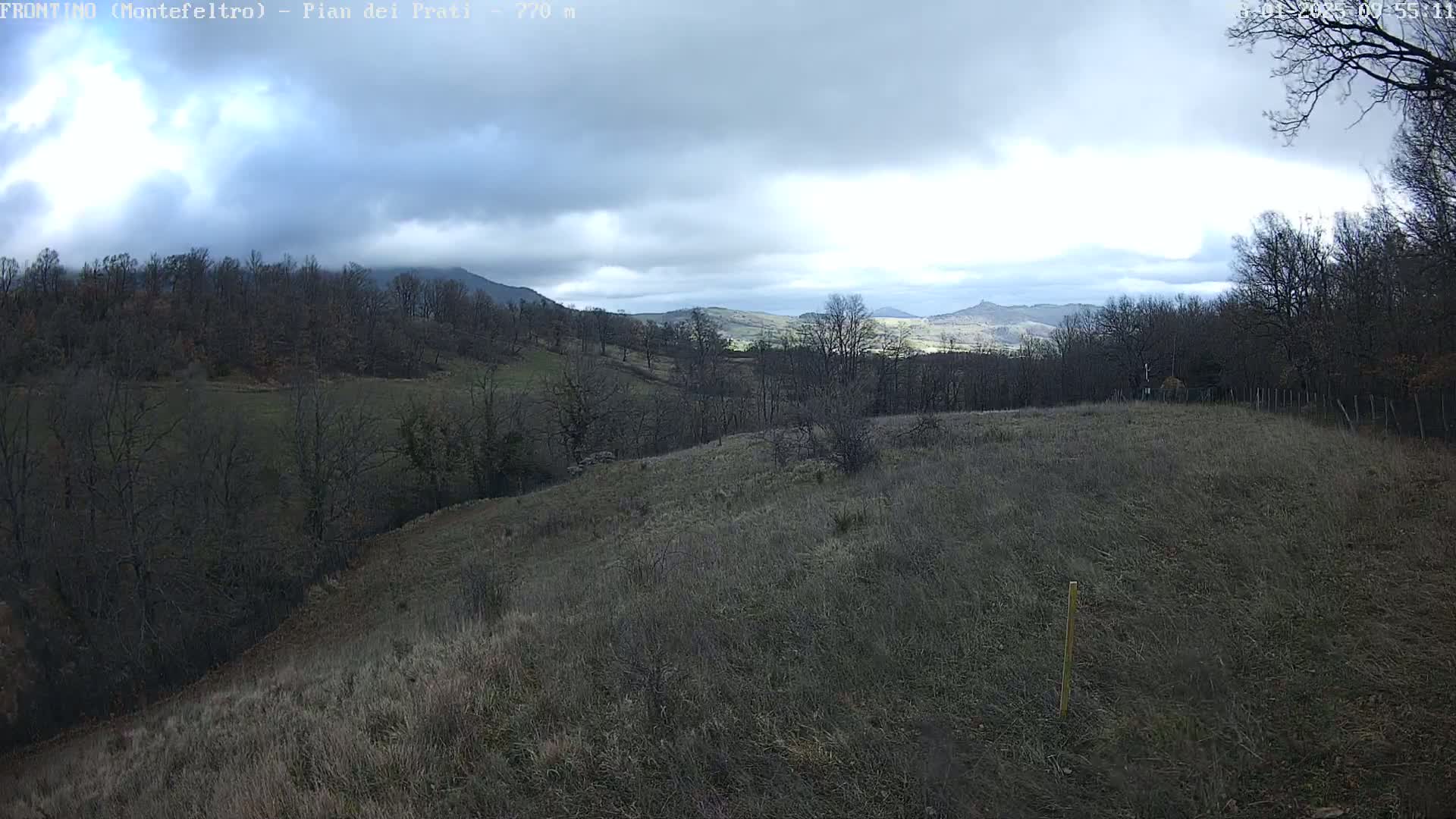 A mostly cloudy day reveals a hilly landscape with bare, deciduous trees and dry, brown grass under a partly sunny sky.