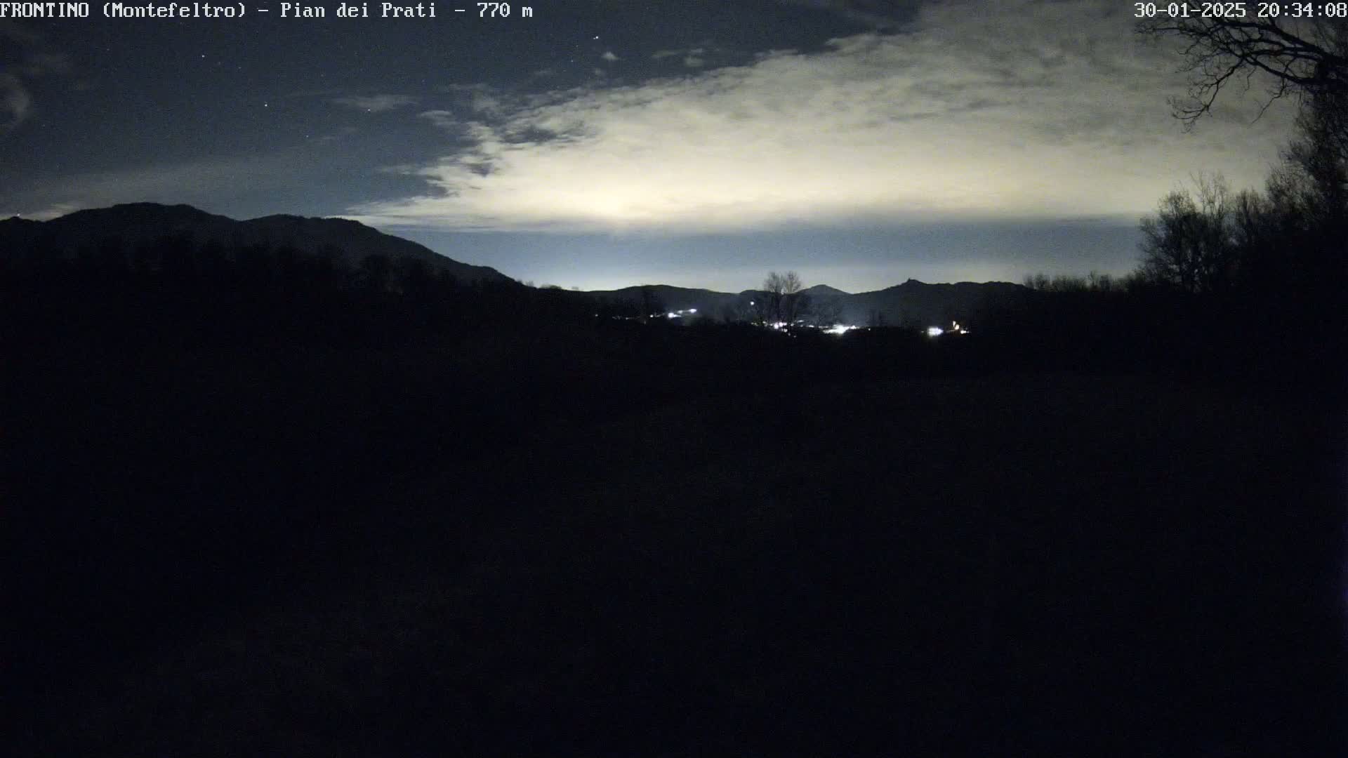 A nighttime view of dimly lit mountains and a dark foreground under a cloudy sky.