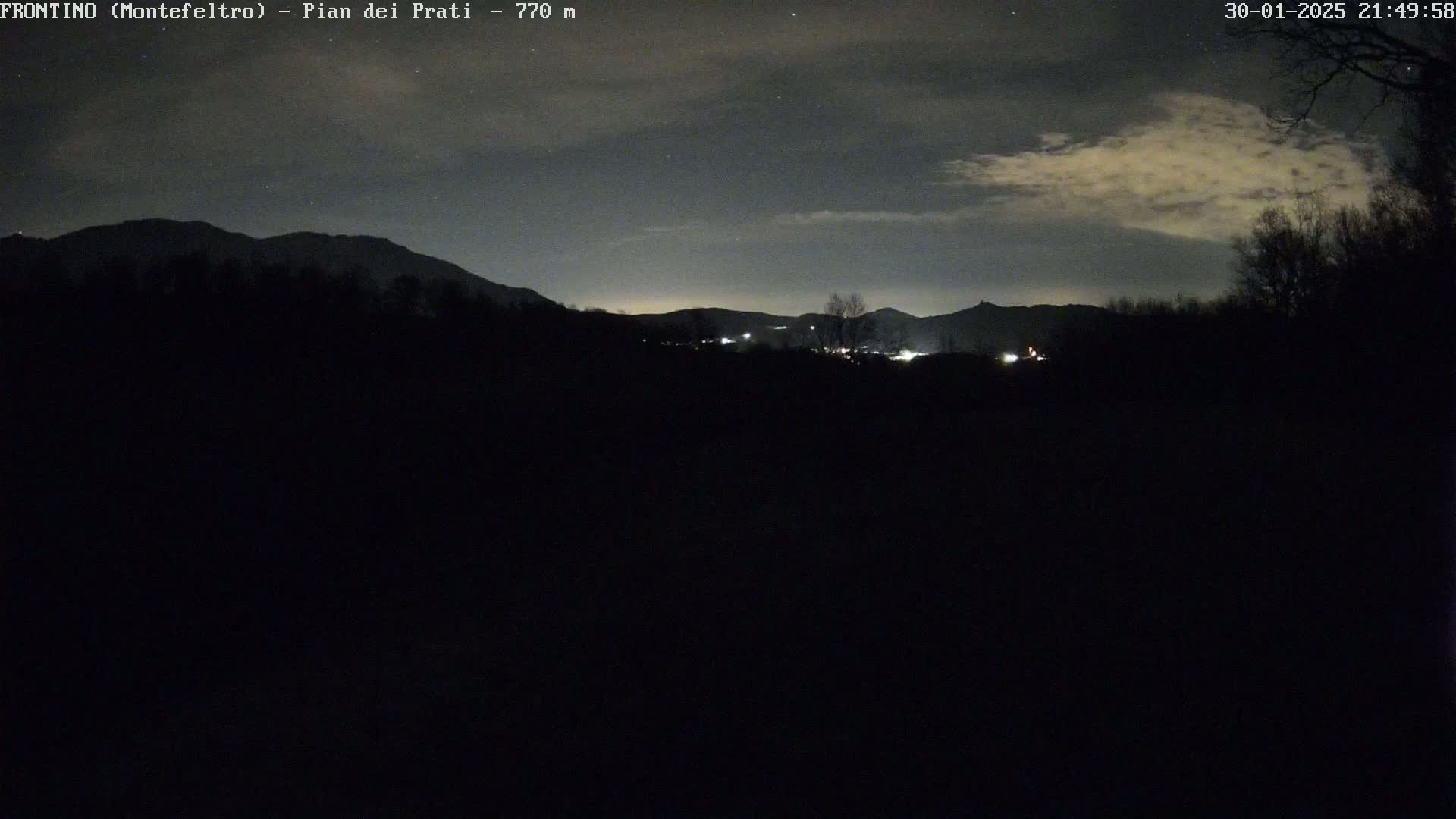 A nighttime view of dimly lit hills and a partly cloudy sky.