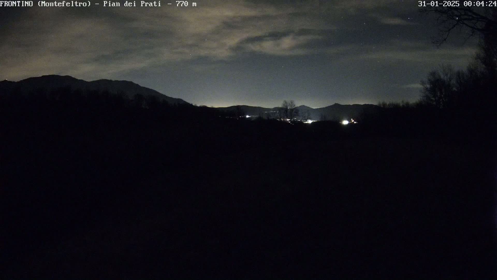 A nighttime view of silhouetted mountains and trees under a partly cloudy sky.