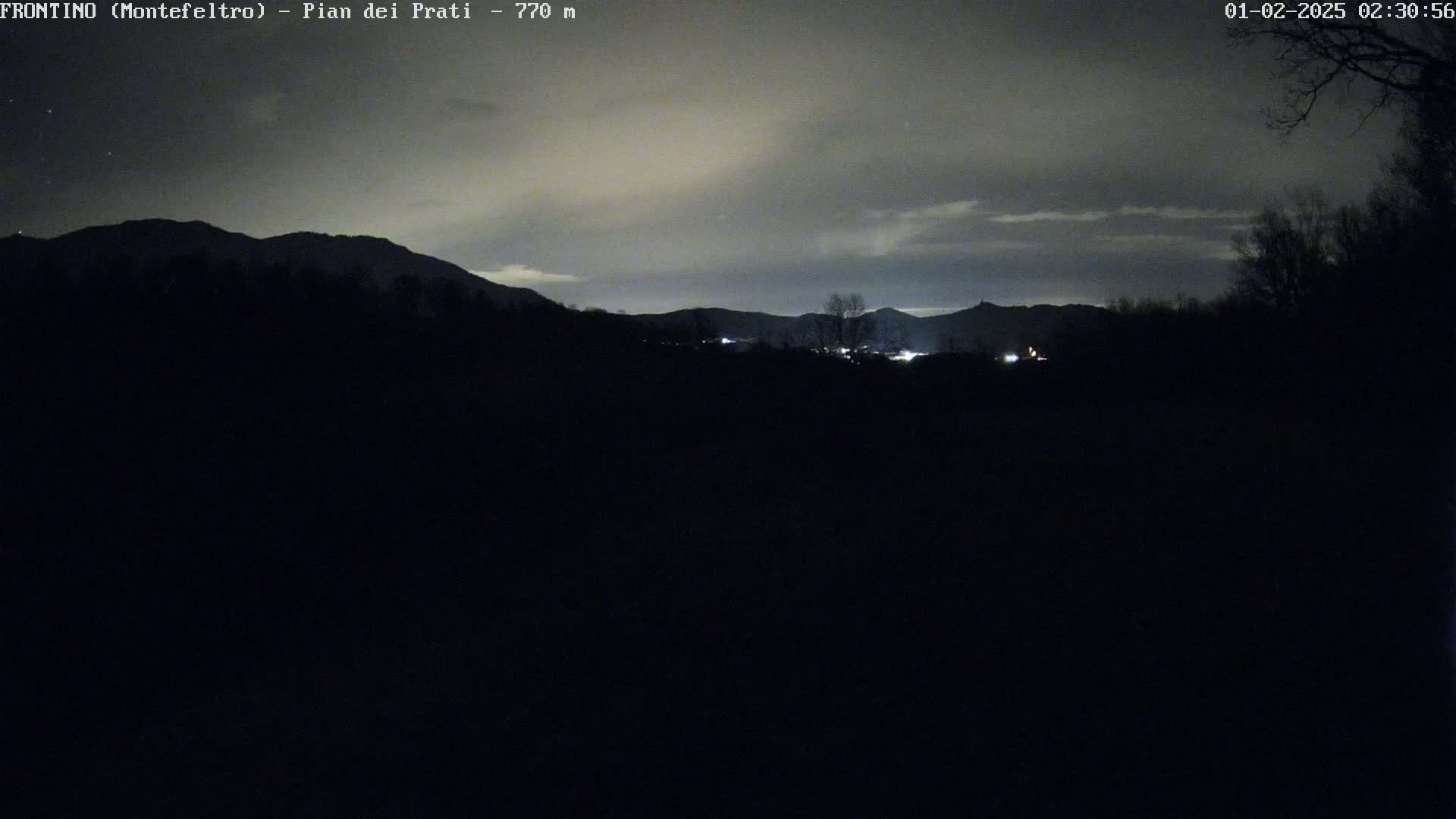 A nighttime, overcast view of distant mountains and a dark foreground, with a few faint lights visible in the middle ground.