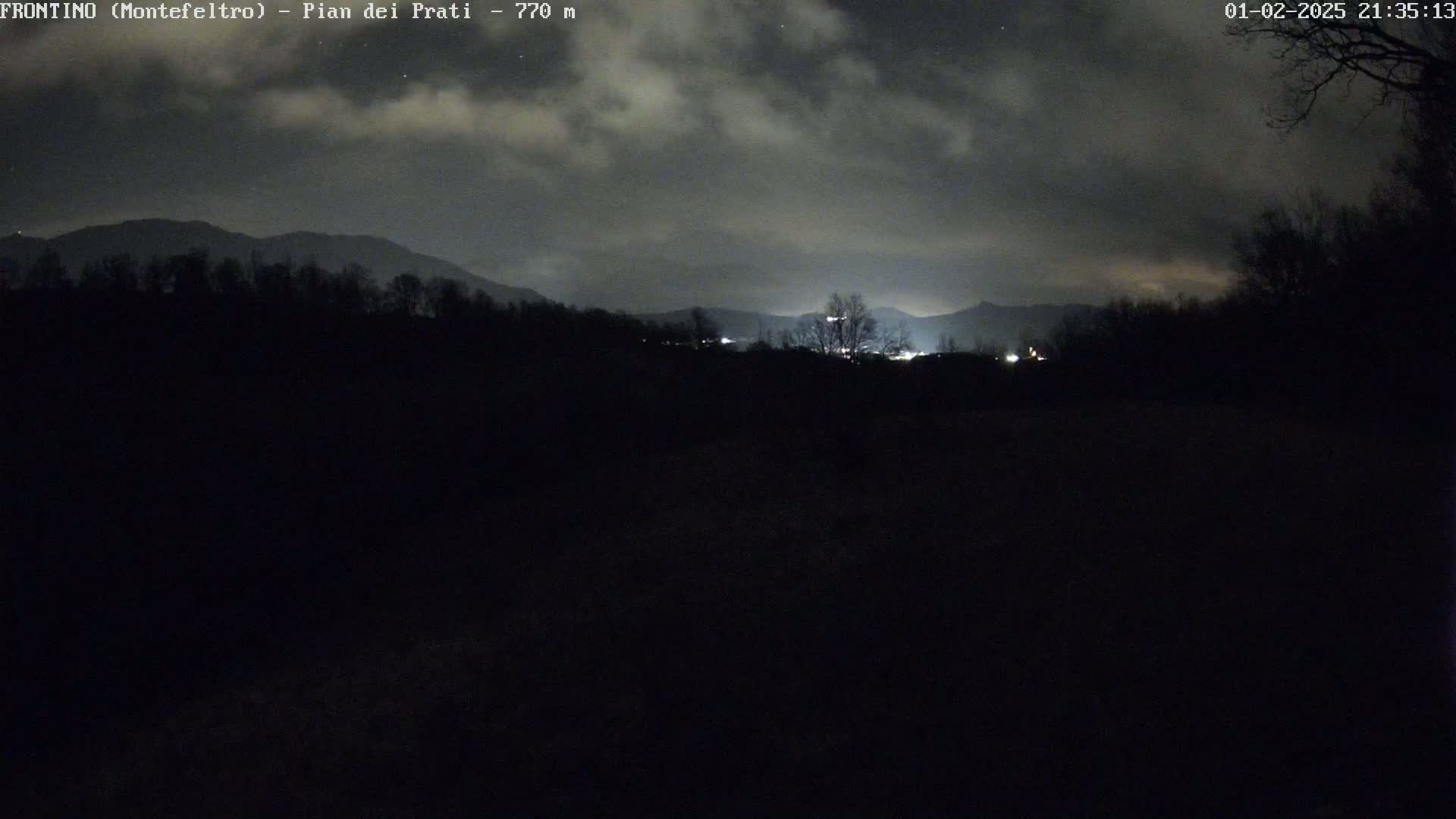 A nighttime view of dark, silhouetted trees and mountains under a cloudy sky.