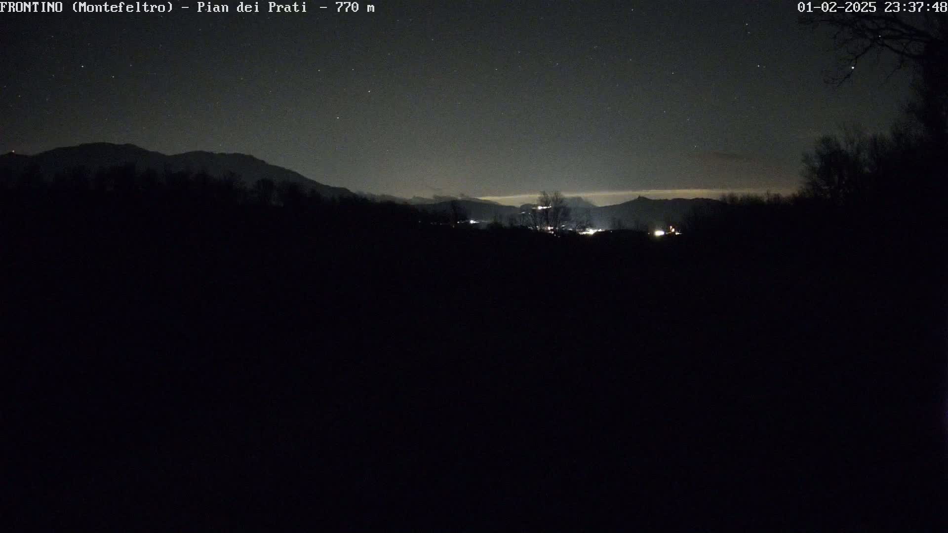 A nighttime view of distant mountains and a small settlement under a clear, starry sky.