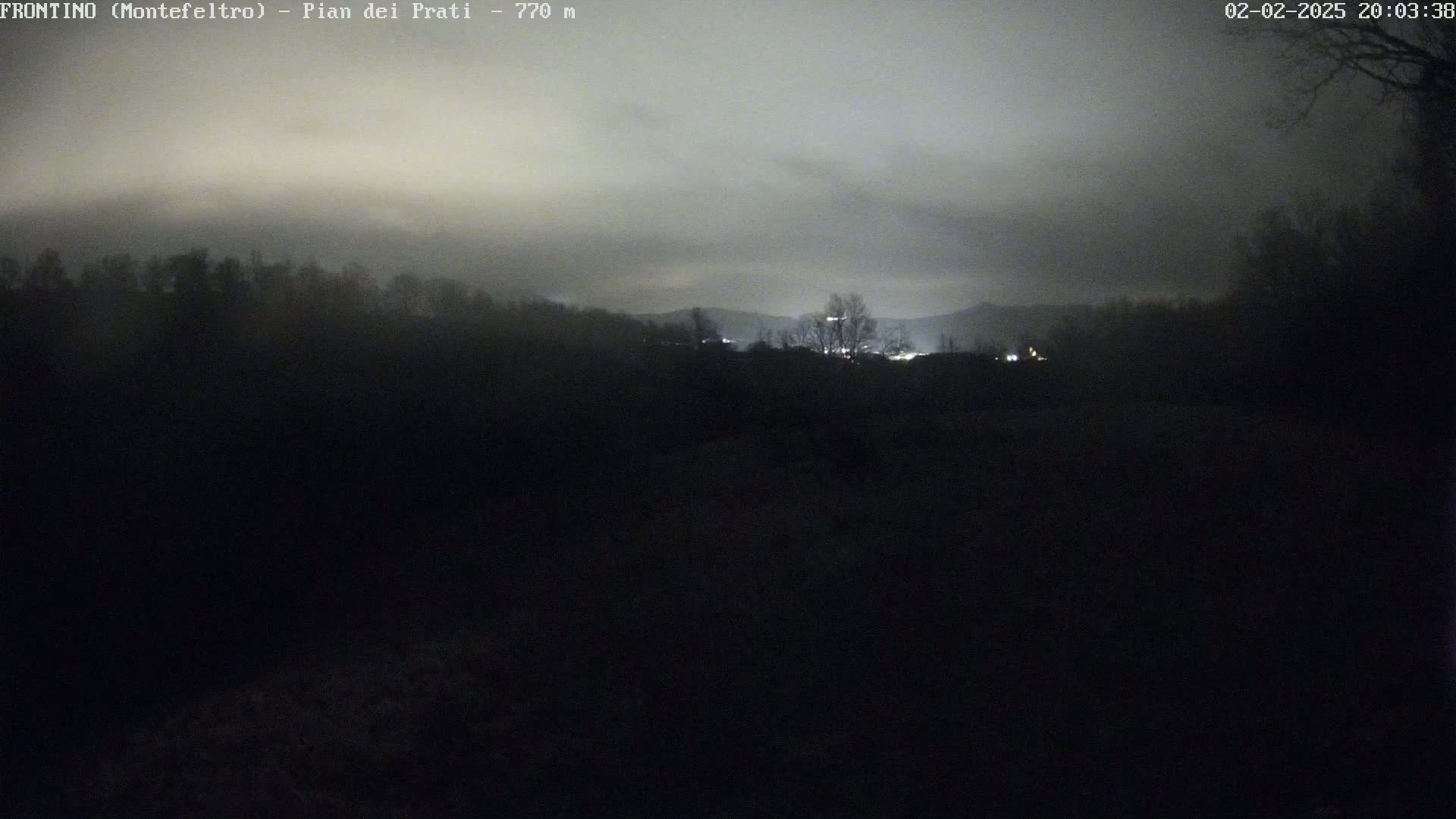 A nighttime view of dimly lit trees and hills under a cloudy sky.