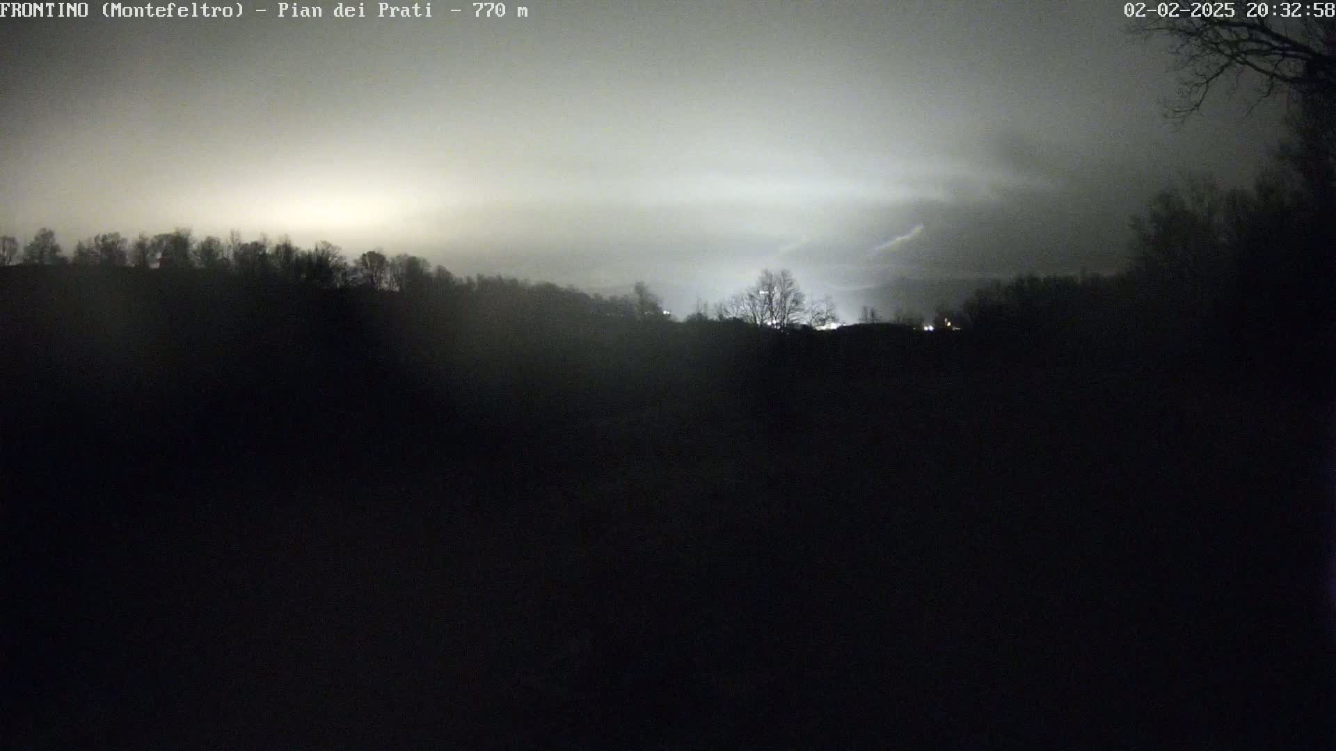A nighttime, foggy view of a dark hillside silhouetted against a faintly illuminated sky.