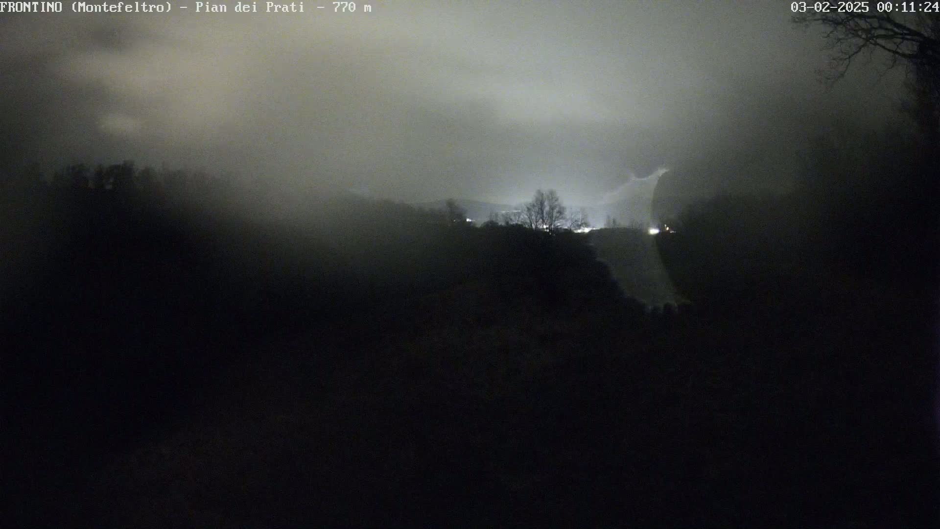 A nighttime view of a foggy hillside with dimly lit areas in the distance.