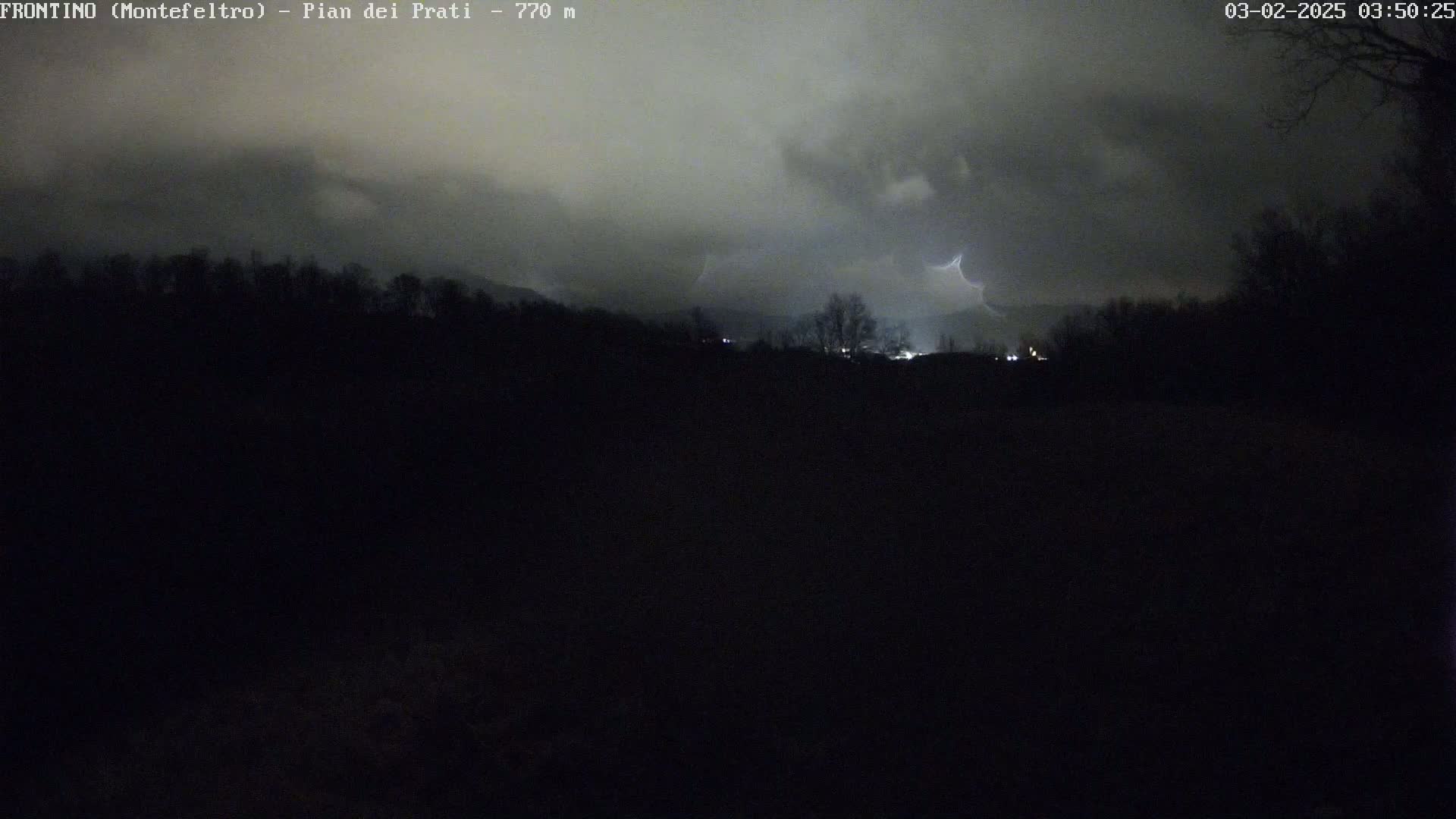 A nighttime, stormy scene shows a dark landscape with distant lightning illuminating a line of trees and hills under a cloudy sky.