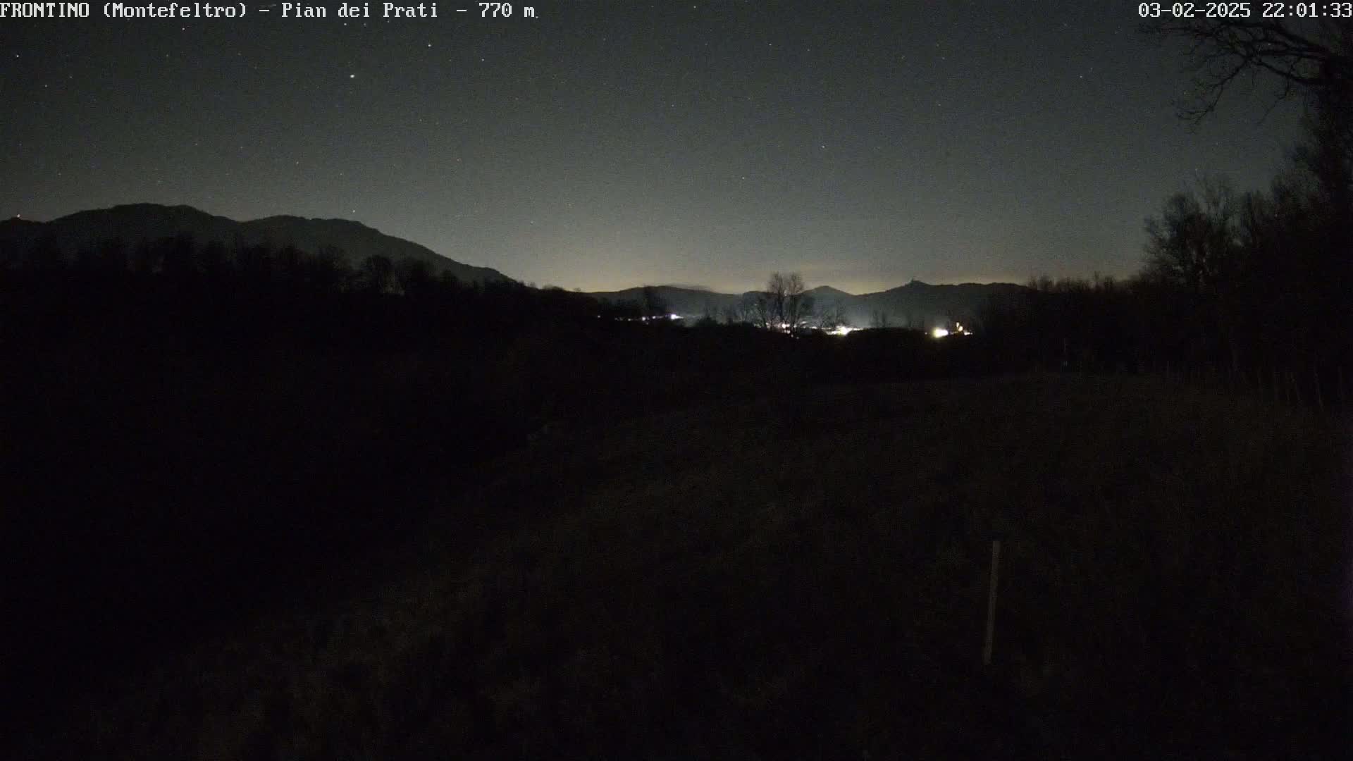 A dark, nighttime landscape shows distant, dimly lit mountains under a clear, starry sky.