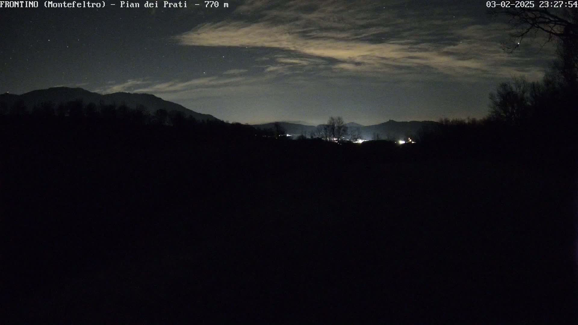 A nighttime view of a dark, mountainous landscape under a partly cloudy sky speckled with stars.