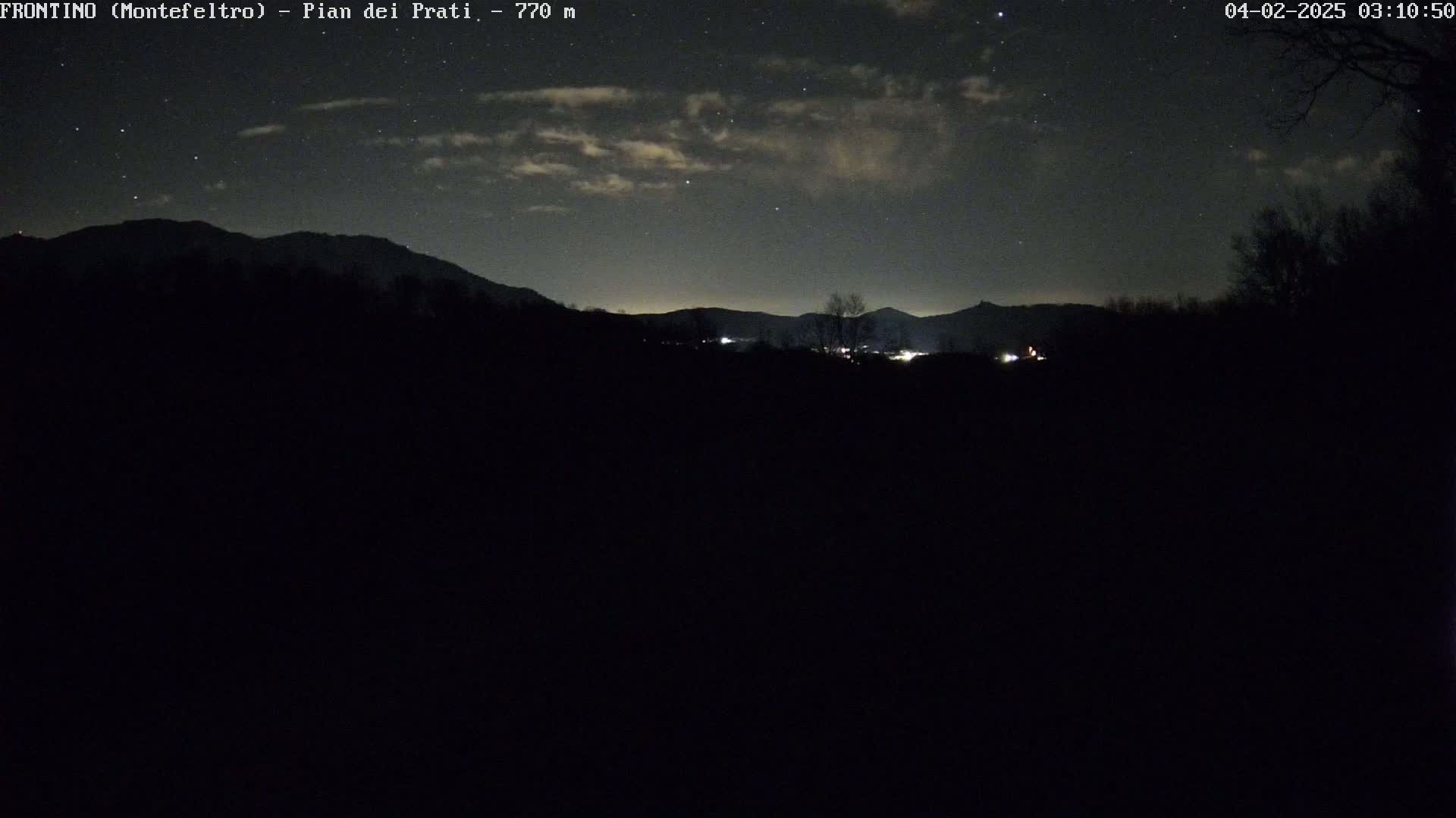 A nighttime view of a dark, mountainous landscape under a partly cloudy sky with some stars visible.