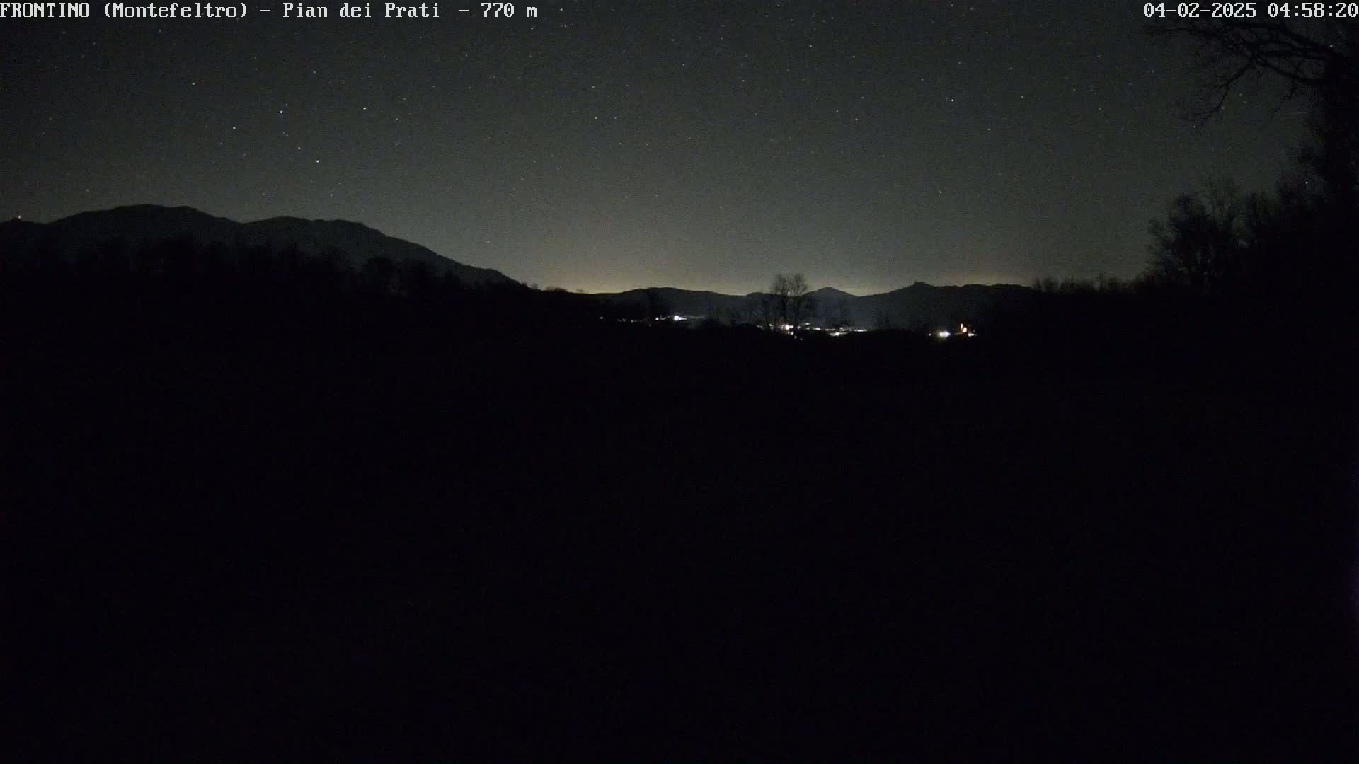 A dark, starlit night scene shows a silhouetted mountain range and a few distant lights.